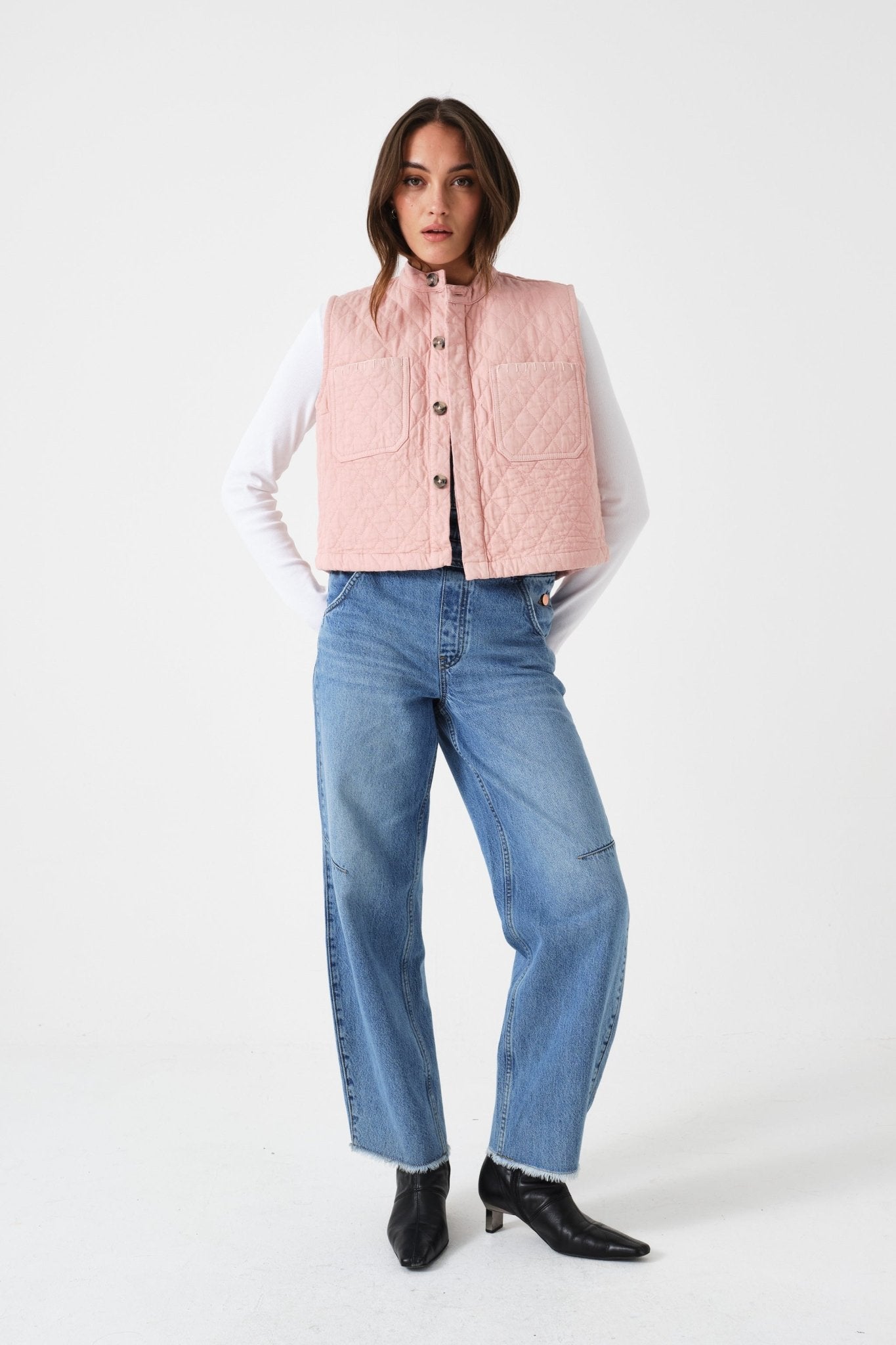 Woman wearing a pink quilted vest, white shirt, blue jeans, and black shoes