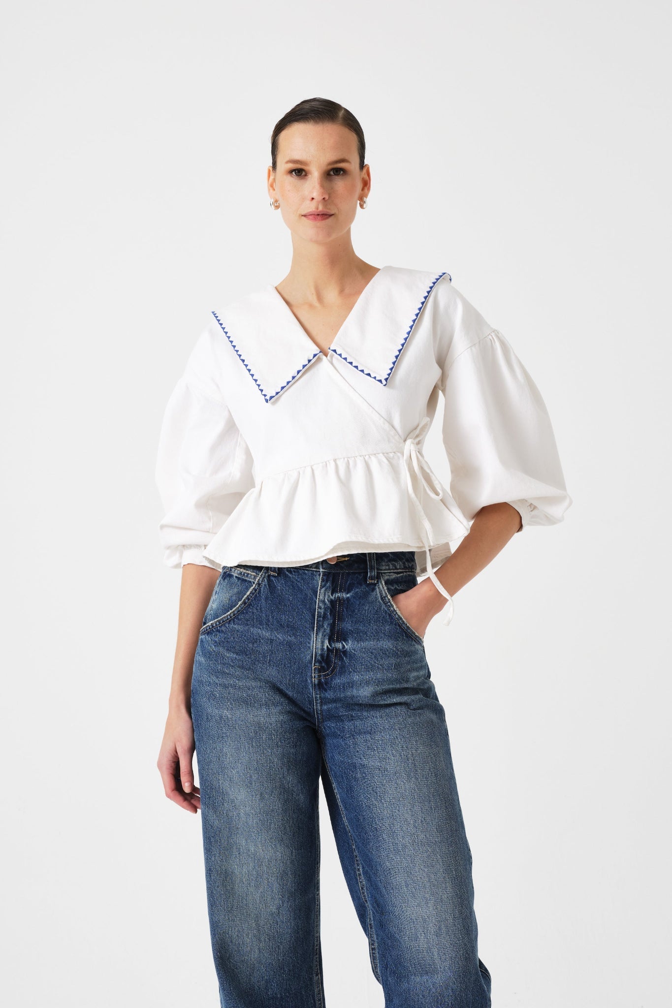 Woman wearing a white blouse with blue trim and blue jeans