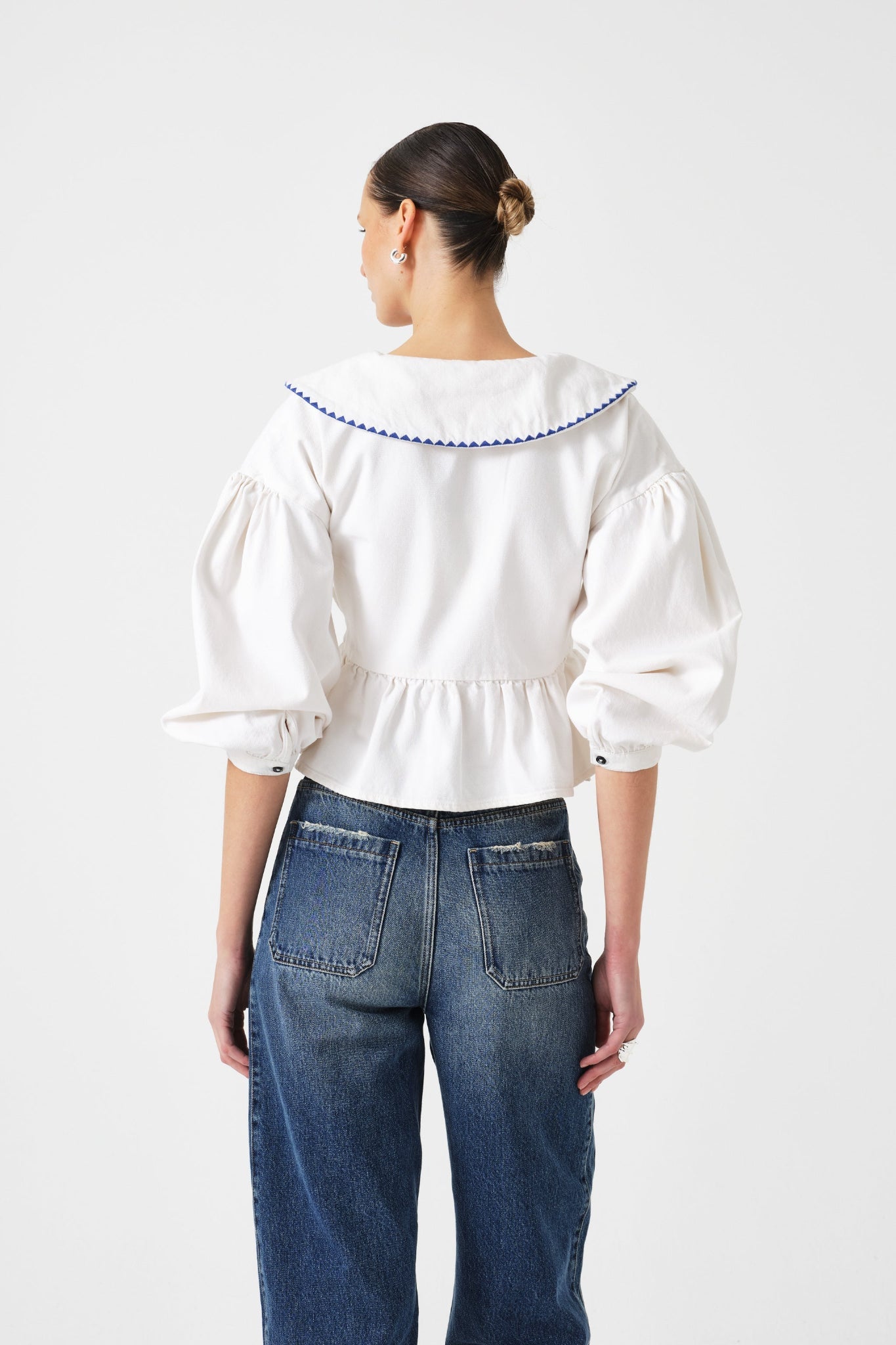 Woman wearing a white wrap blouse with blue trim on collar and long sleeves pushed up