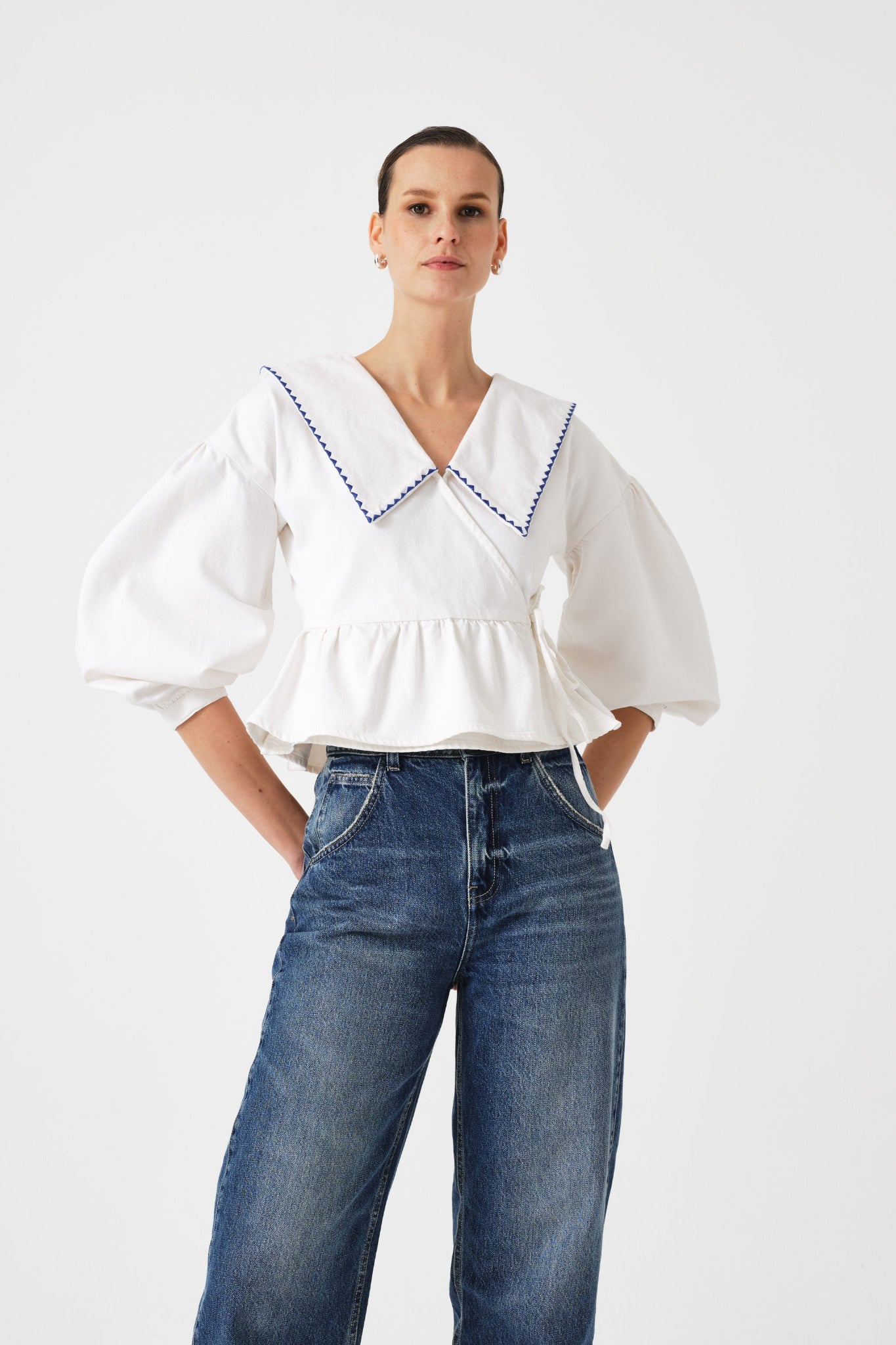 Woman wearing a white wrap blouse tied at the side with blue trim on collar