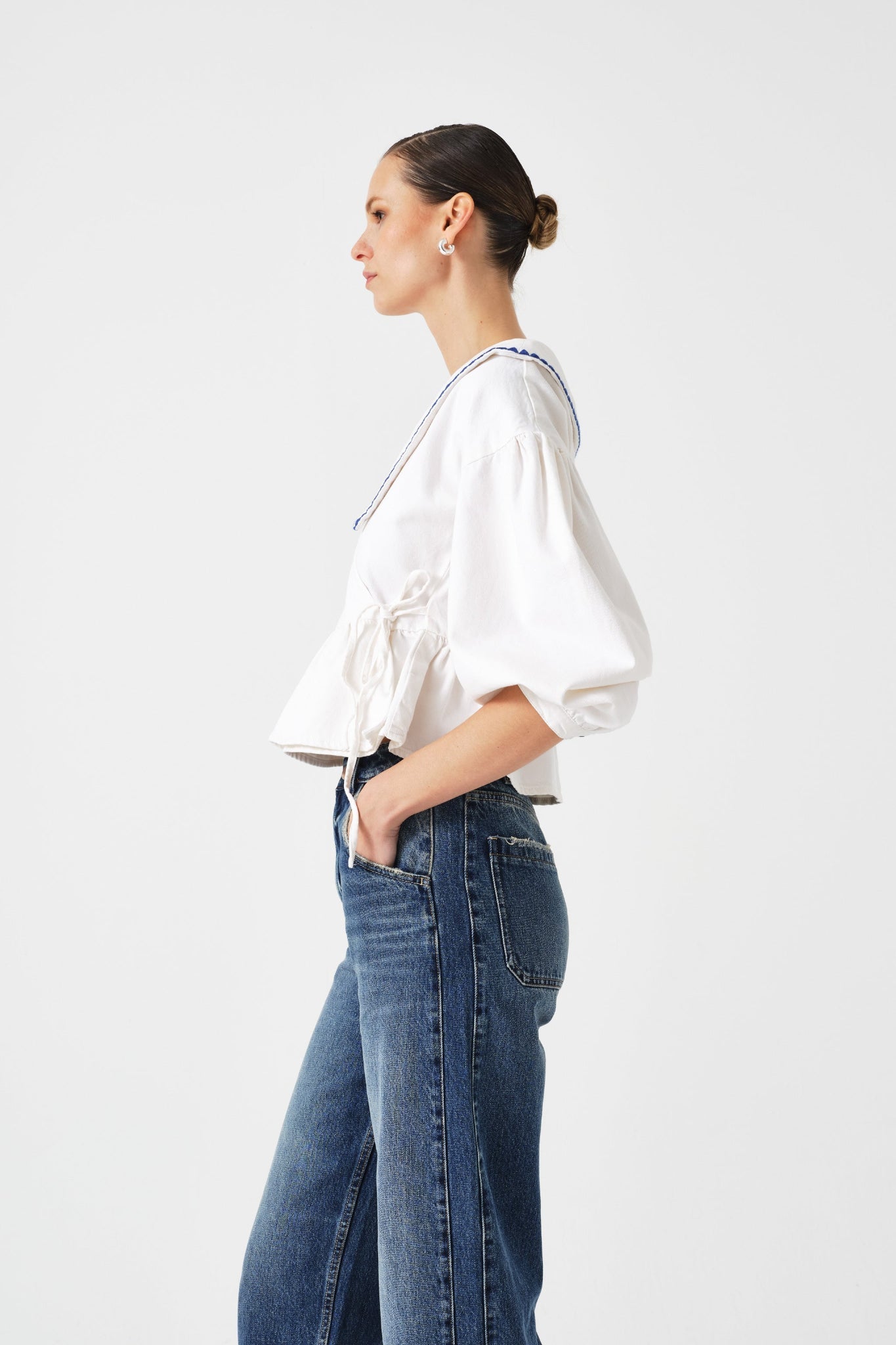 Side view of woman wearing a white wrap blouse and blue jeans with hands in pockets