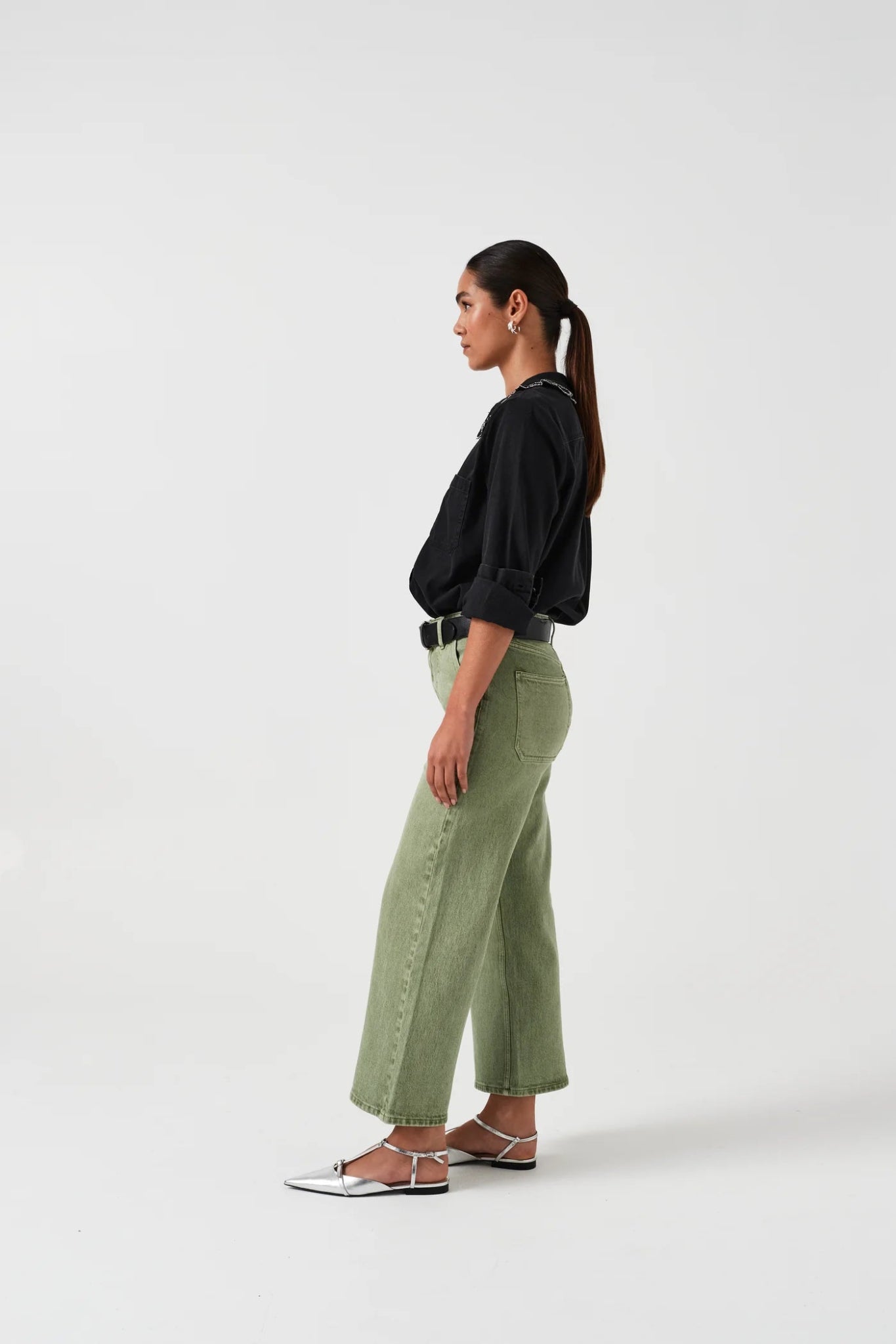 Woman wearing green cropped jeans, a black shirt and sandals standing on the side.