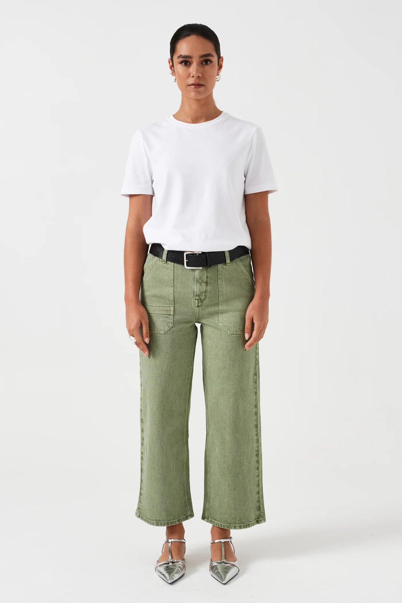 Woman wearing cropped green jeans with pockets and a black belt through loops with a white tee and sandals.