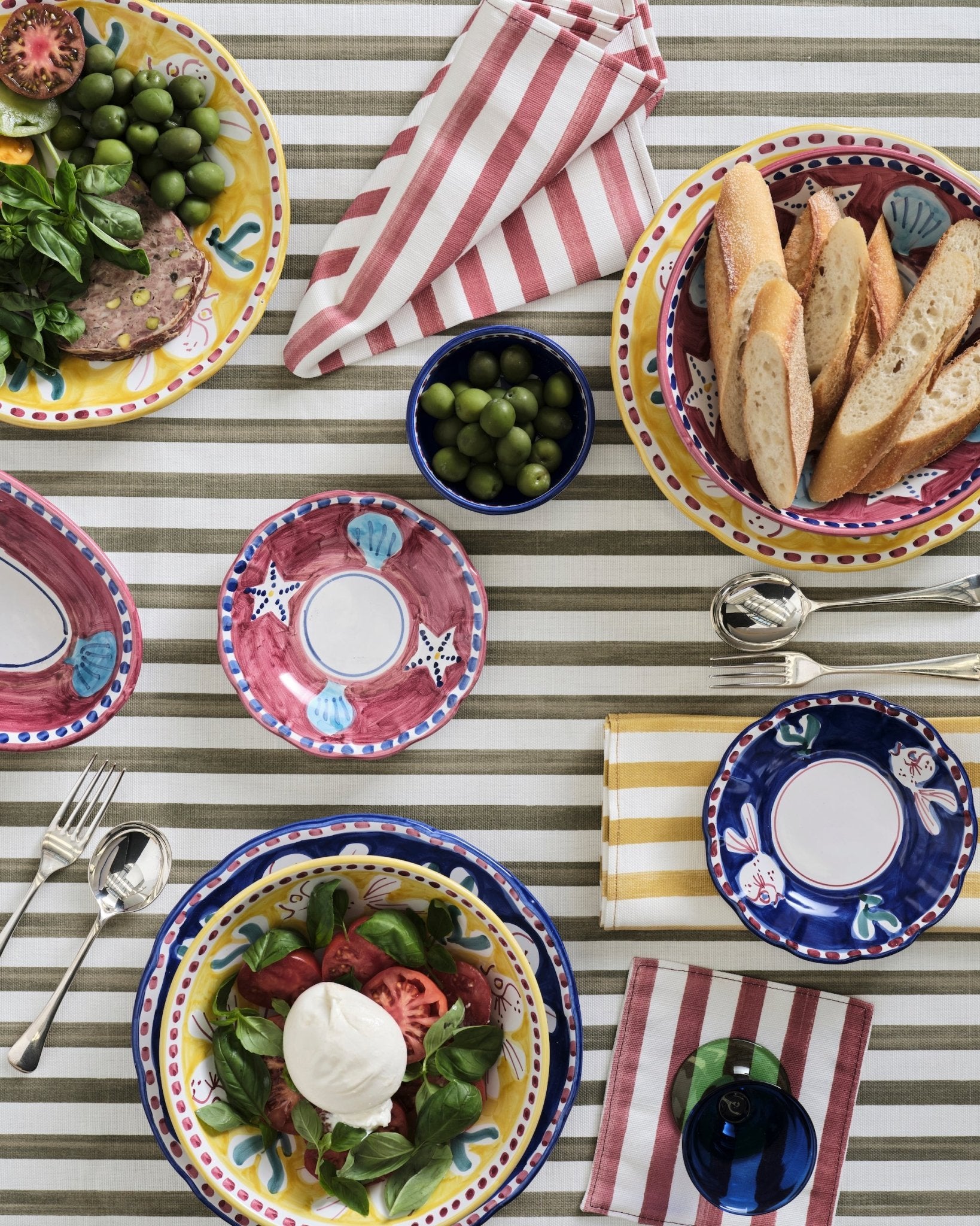 Various coloured striped Napkins on an olive striped tablecloth iin a table setting - ANNIE.G