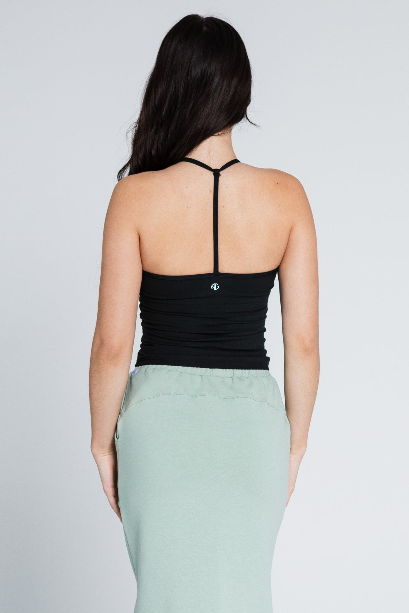 Back of a woman wearing a black sleeveless workout top and green skirt with elastic waist.