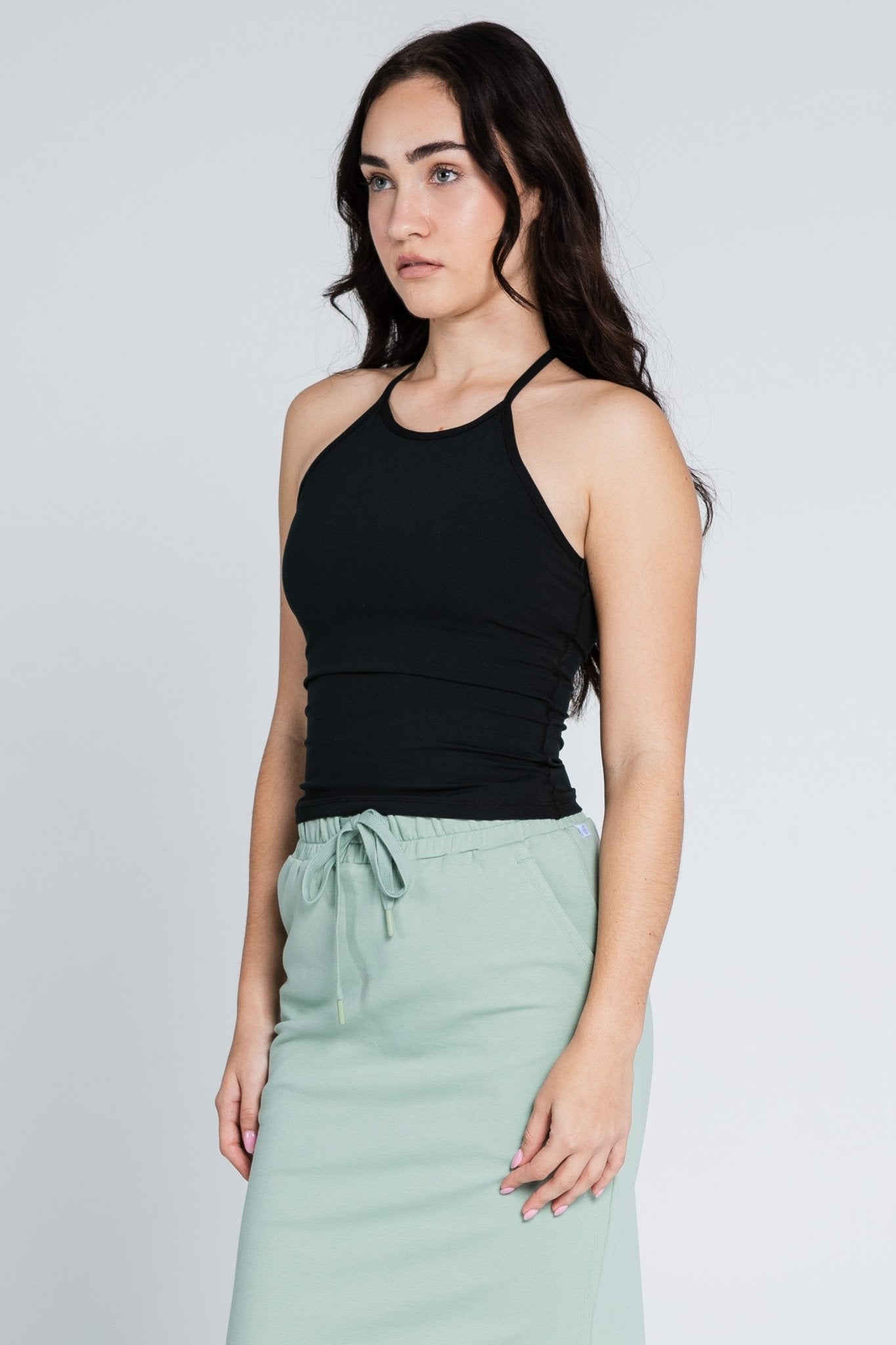 Side of a woman wearing a black sleeveless workout top and green skirt with elastic waist and drwastring.