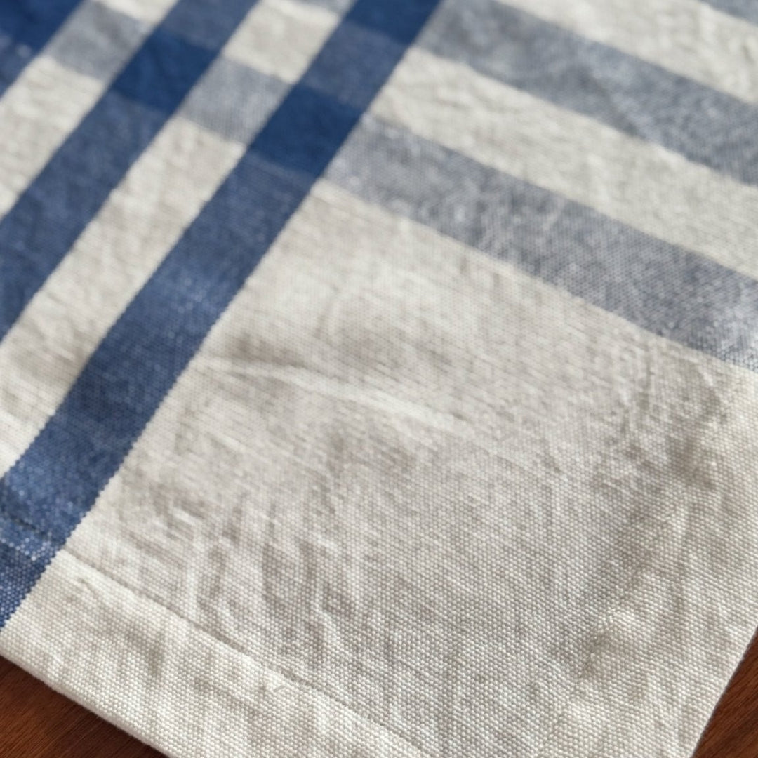 Close-up of a rectangular tablecloth with blue and white checks and hemmed edge on a wooden table.