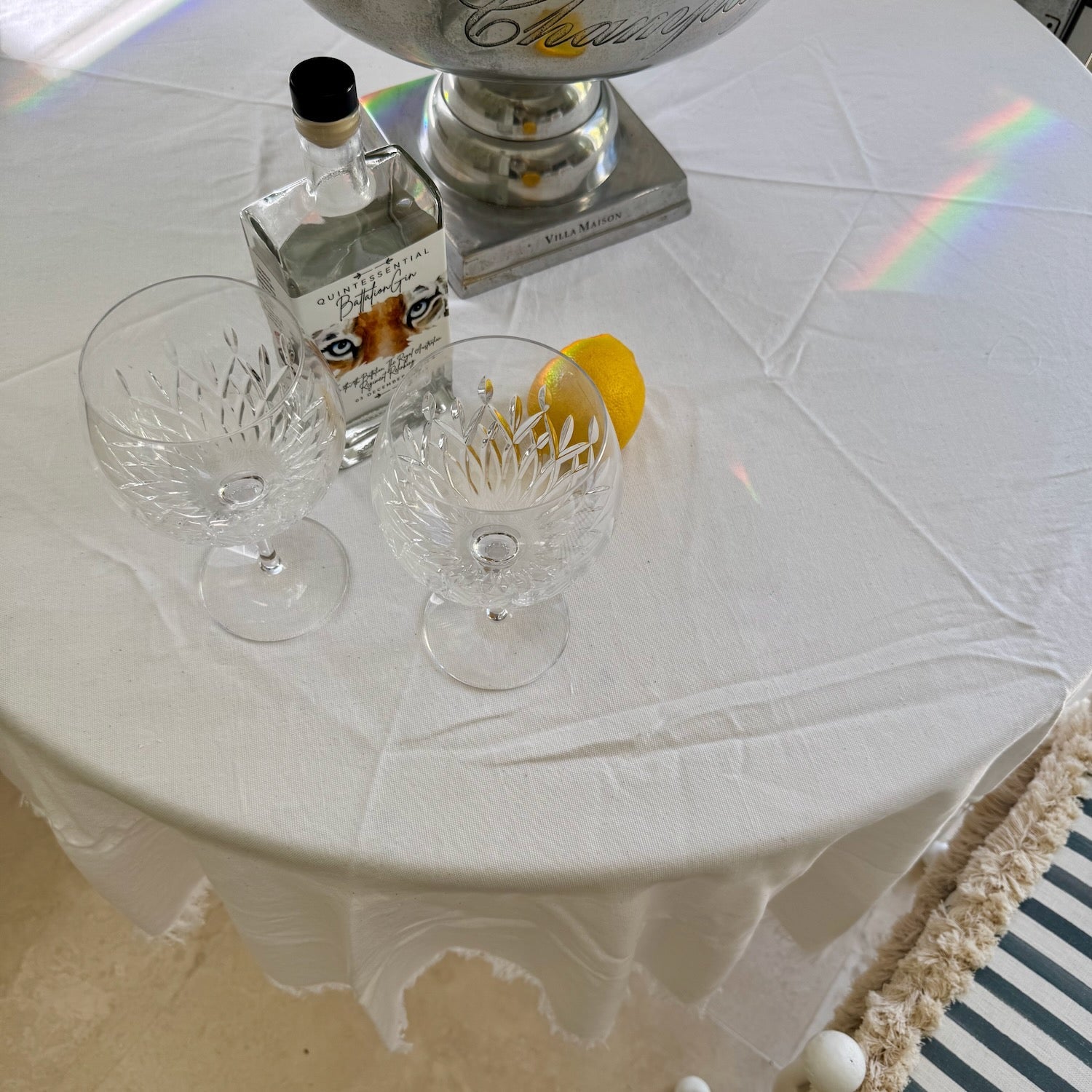 white round tablecloth on a pedestal table with an alcohol bottle, a lemon and two glasses on a round table