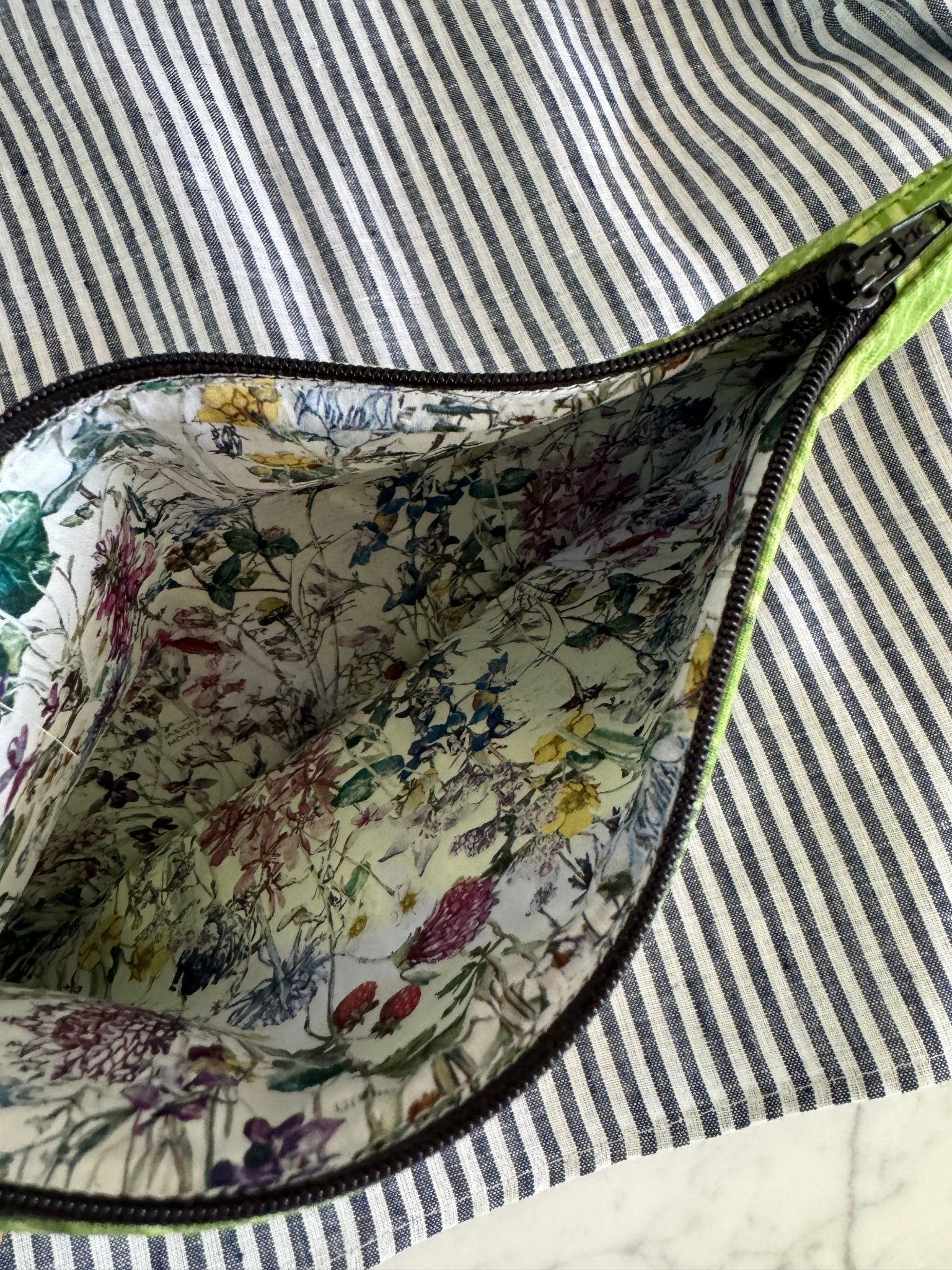 Zip open on navy striped pouch showing inside floral lining and sitting on a navy stripe blouse.