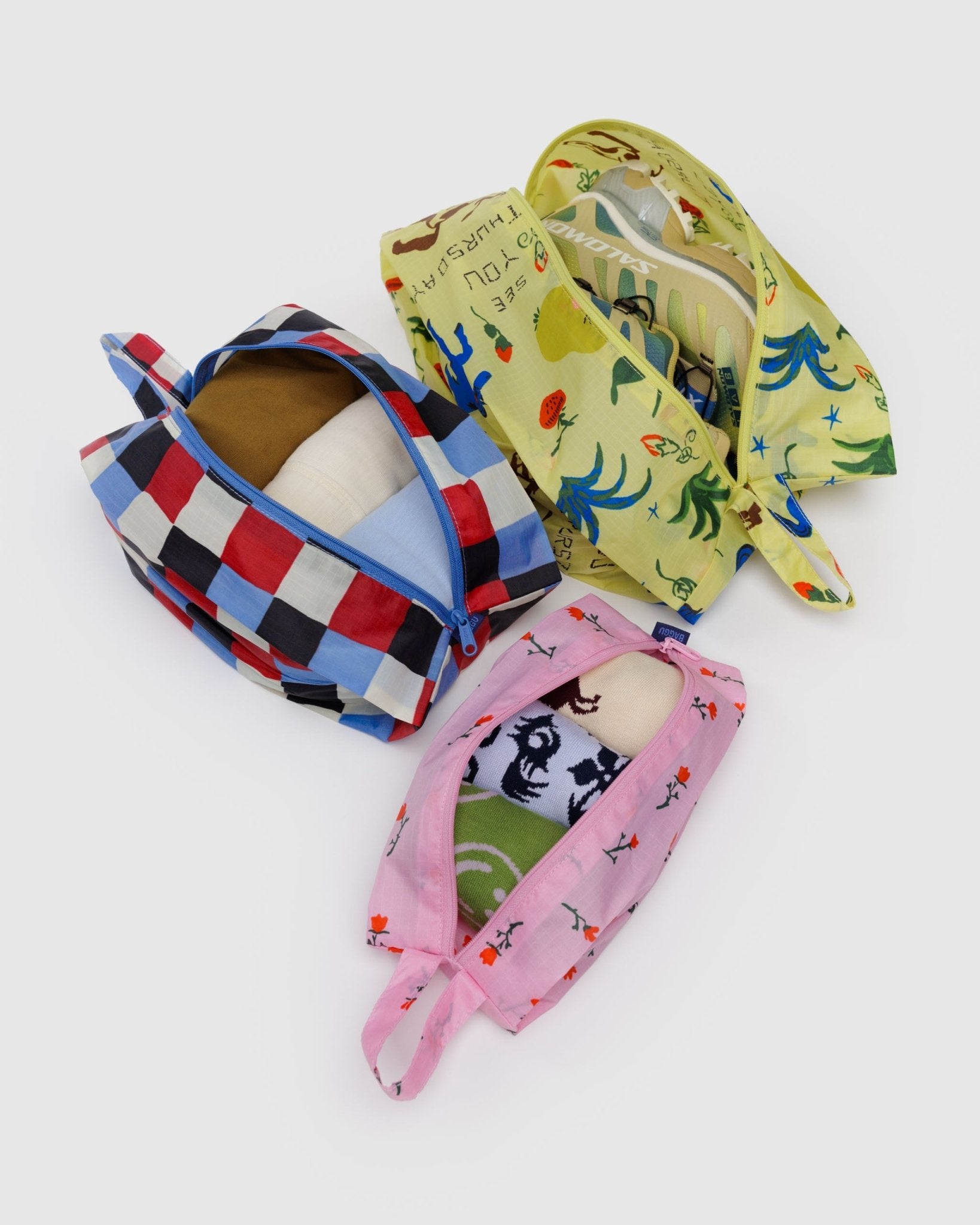 Three different sized, colourful zip bags with hanging loops in different prairie patterns filled with clothing and shoes.