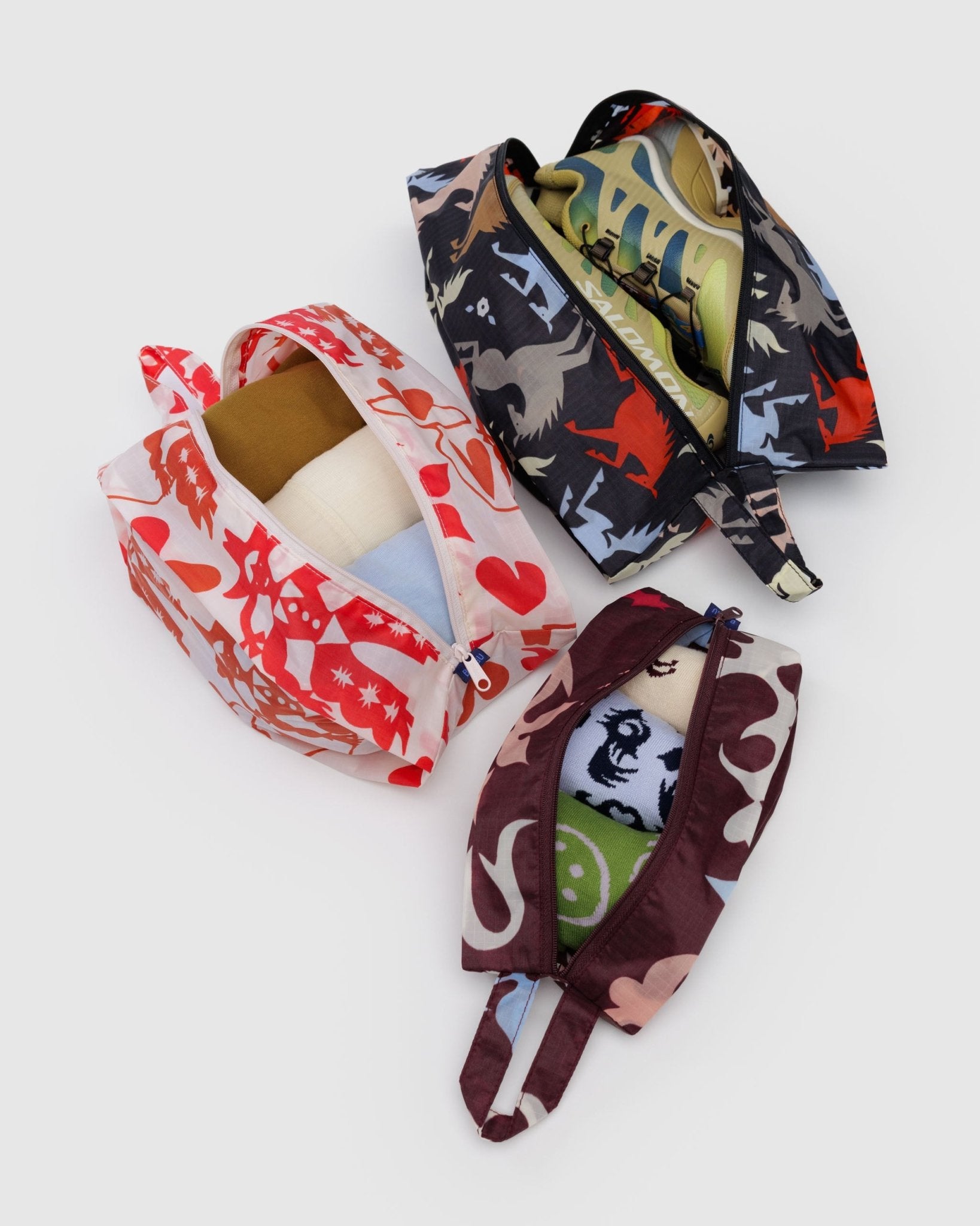 Set of 3 expandable zip top bags in western prints with shoes and clothes inside and a loop tab for hanging or carrying.