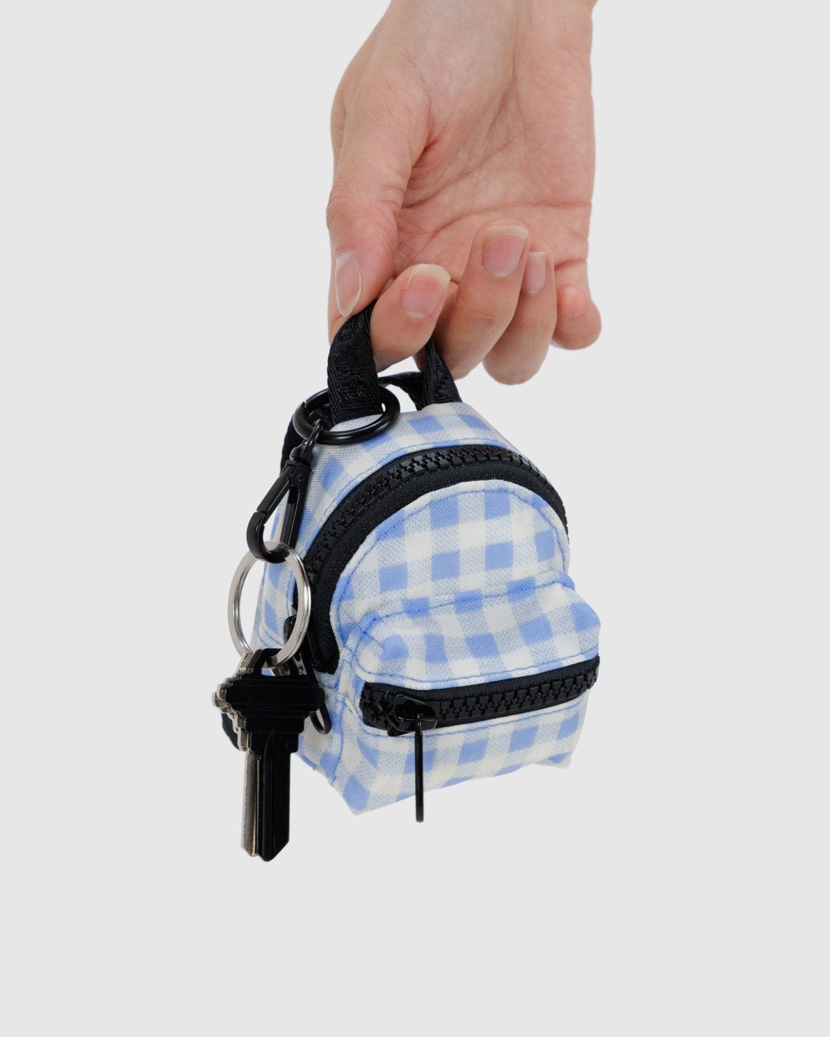Persons hand holding a light blue gingham Baggu Backpack Charm with keys attached to keyring - ANNIE.G