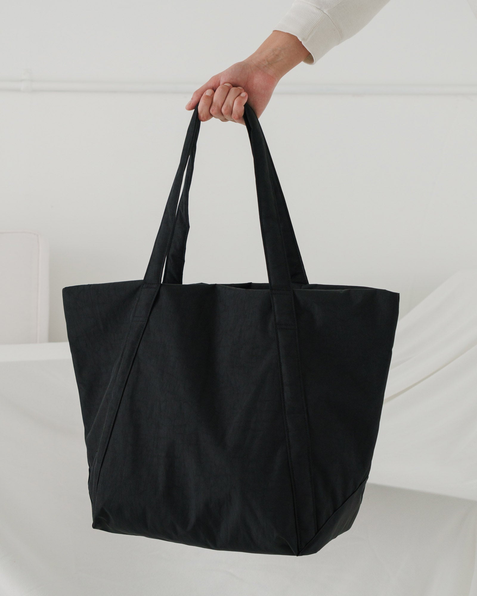 Side view of a black hobo tote bag in trapezoid shape being held by a person's hand.
