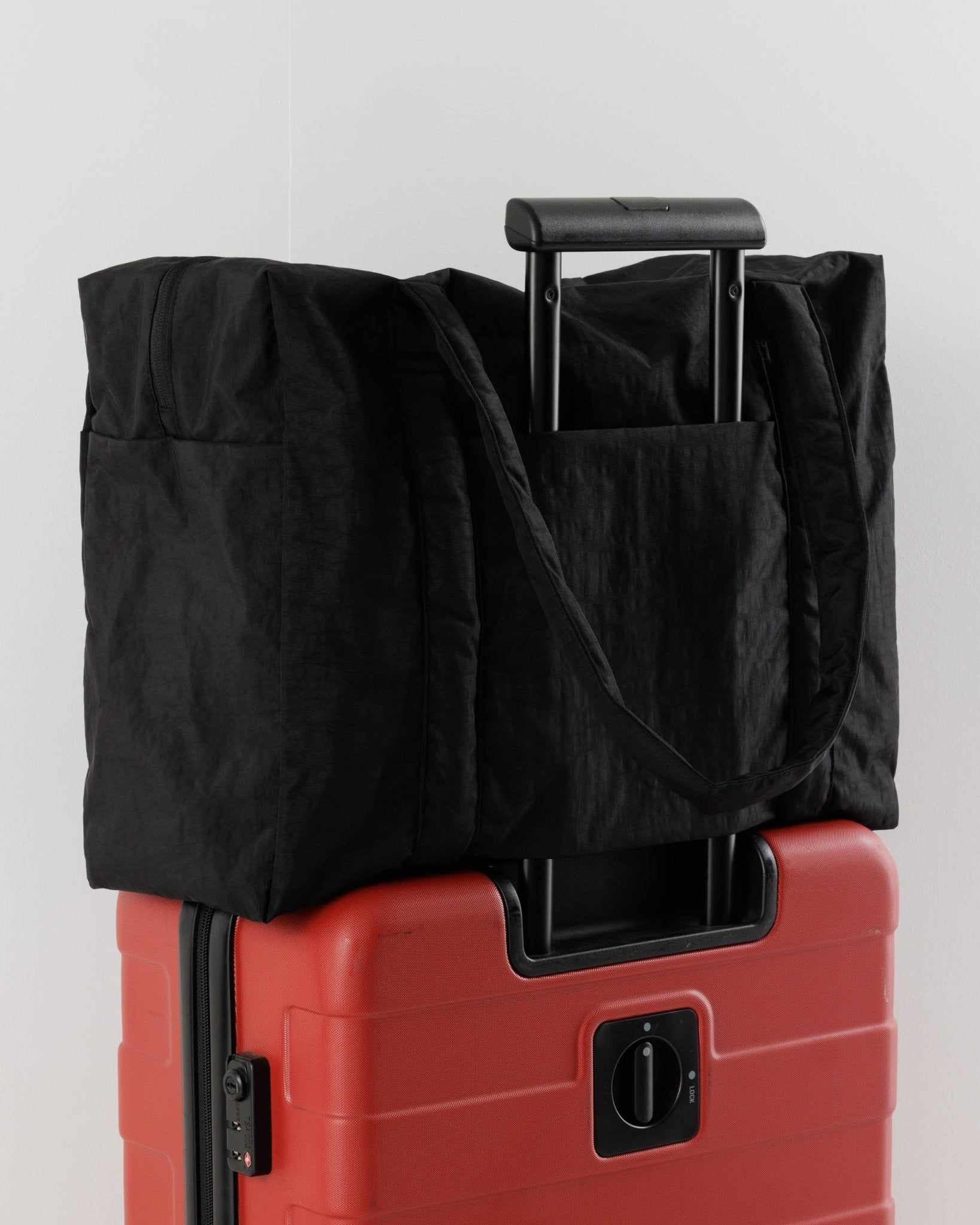 Black duffle bag with luggage sleeve over handle of a red suitcase - ANNIE.G