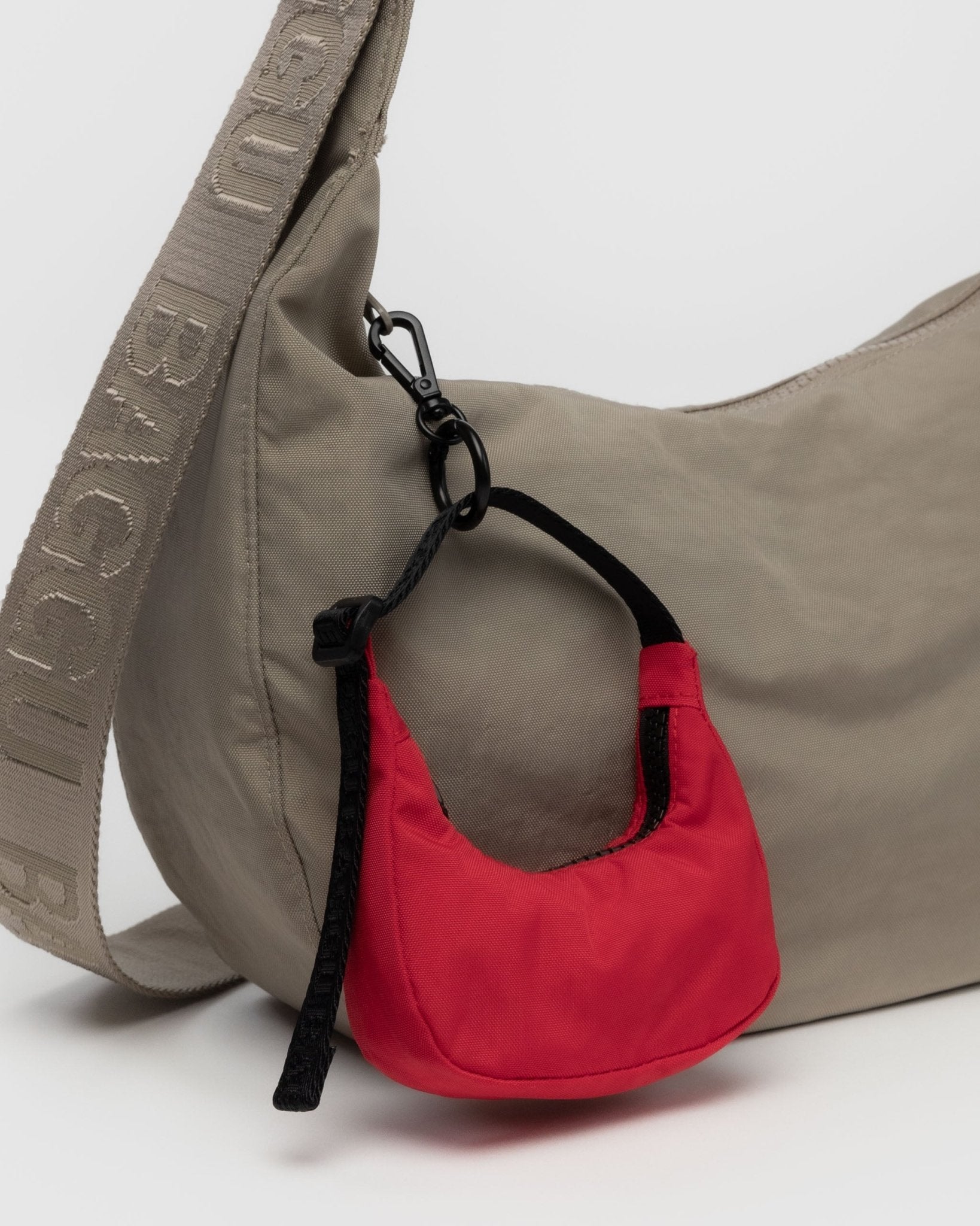 Red crescent shaped bag charm attached to the zip of a beige crescent bag - ANNIE.G