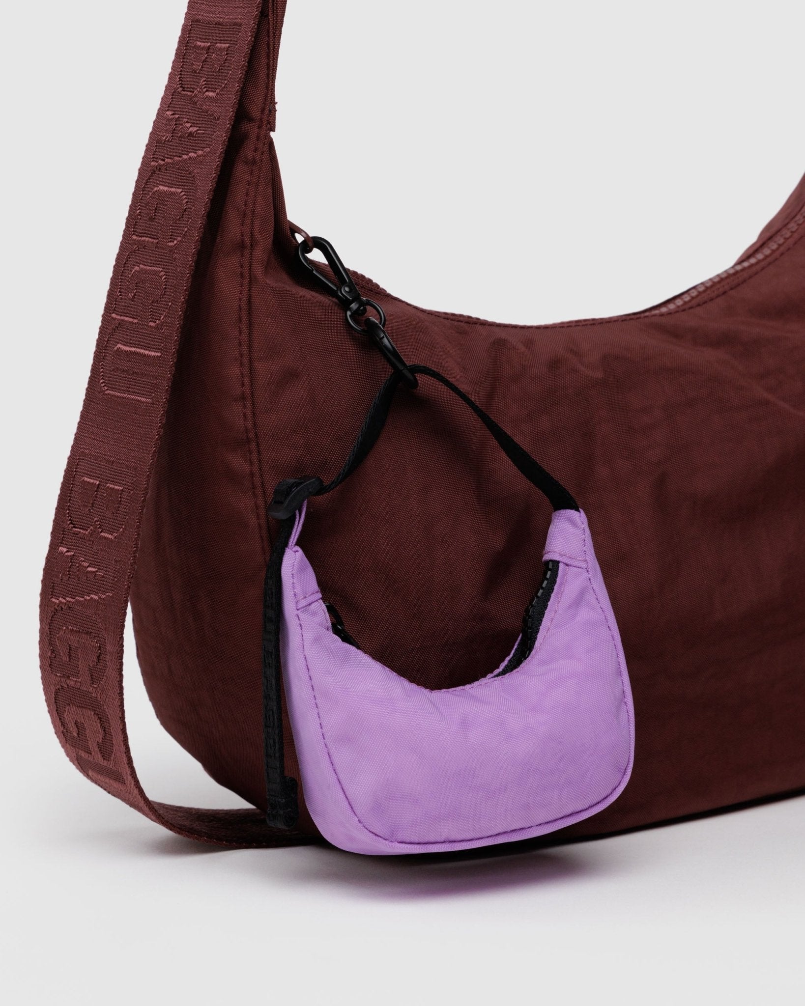 Pink crescent shaped bag charm attached to a burgundy crescent shaped bag.