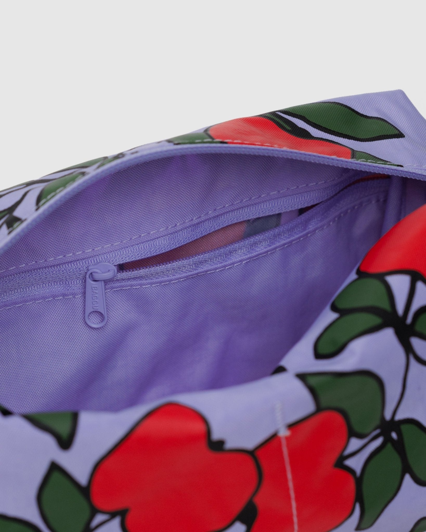 Inside purple lining and zip pouch of of toiletry bag with red apples and green leaves print.