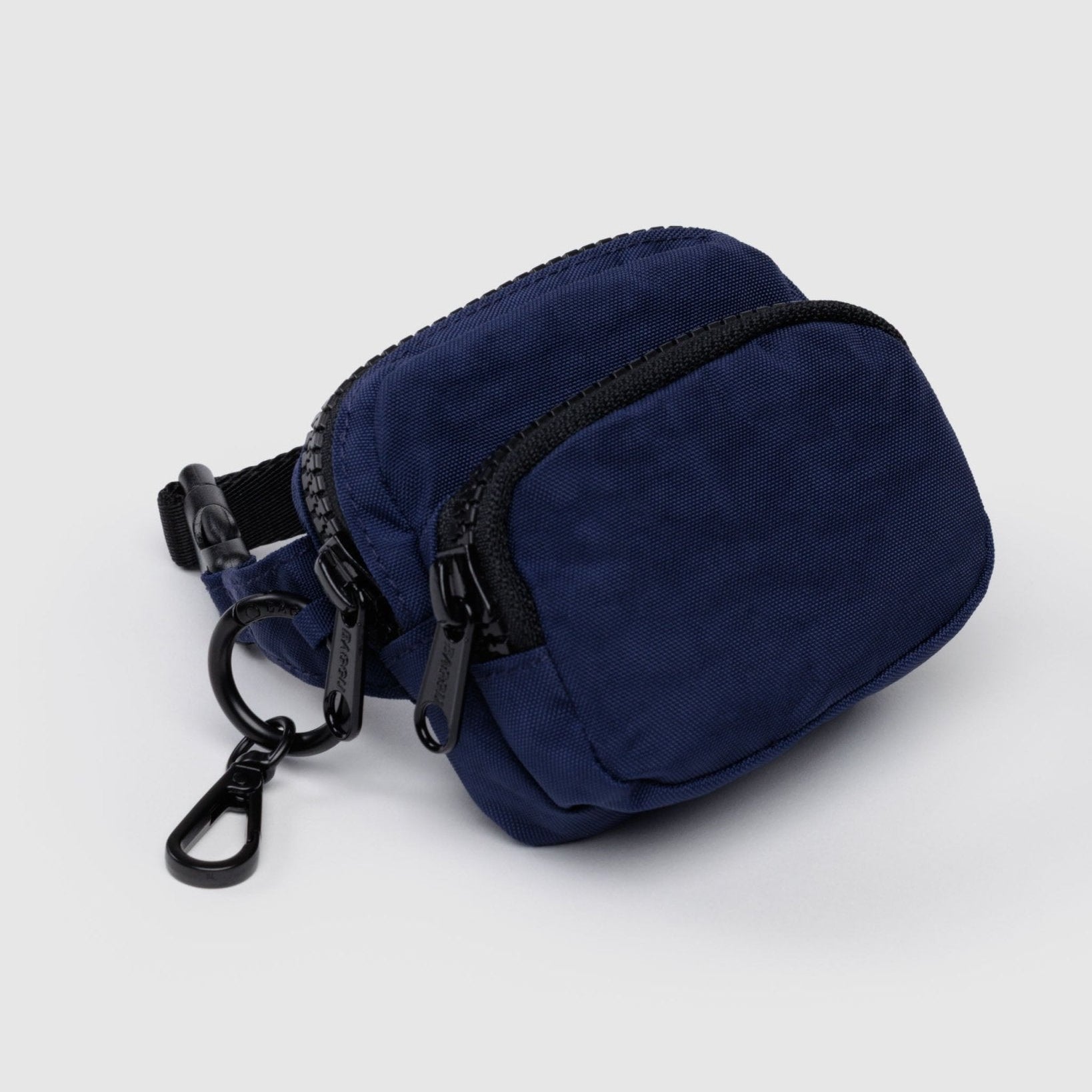 Small, navy blue fanny charm with black zippers on two pockets, a clip and black adjustable strap