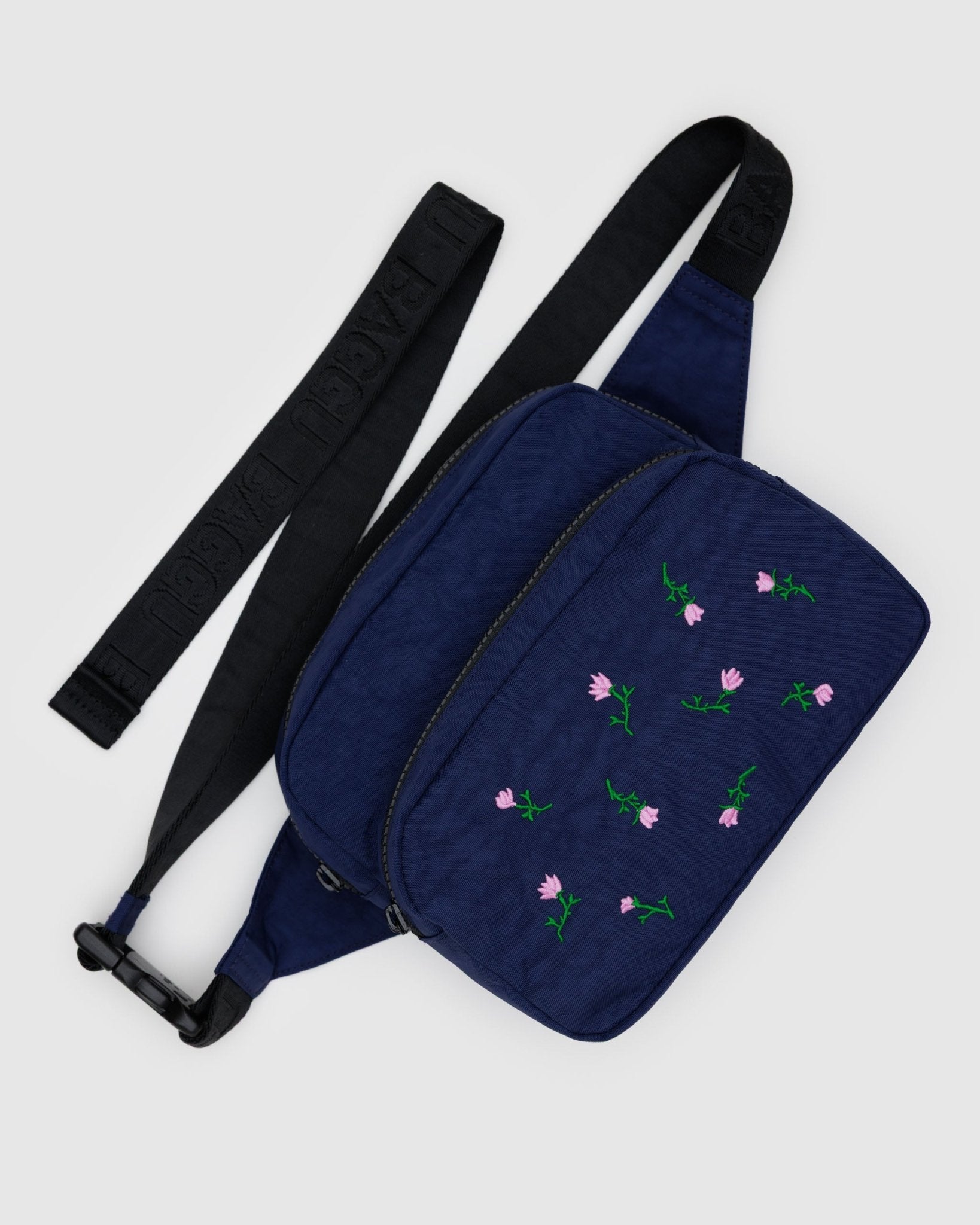 Navy blue fanny pack with adjustable strap and two zip pouches and front pouch is embroidered with pink wildflowers.