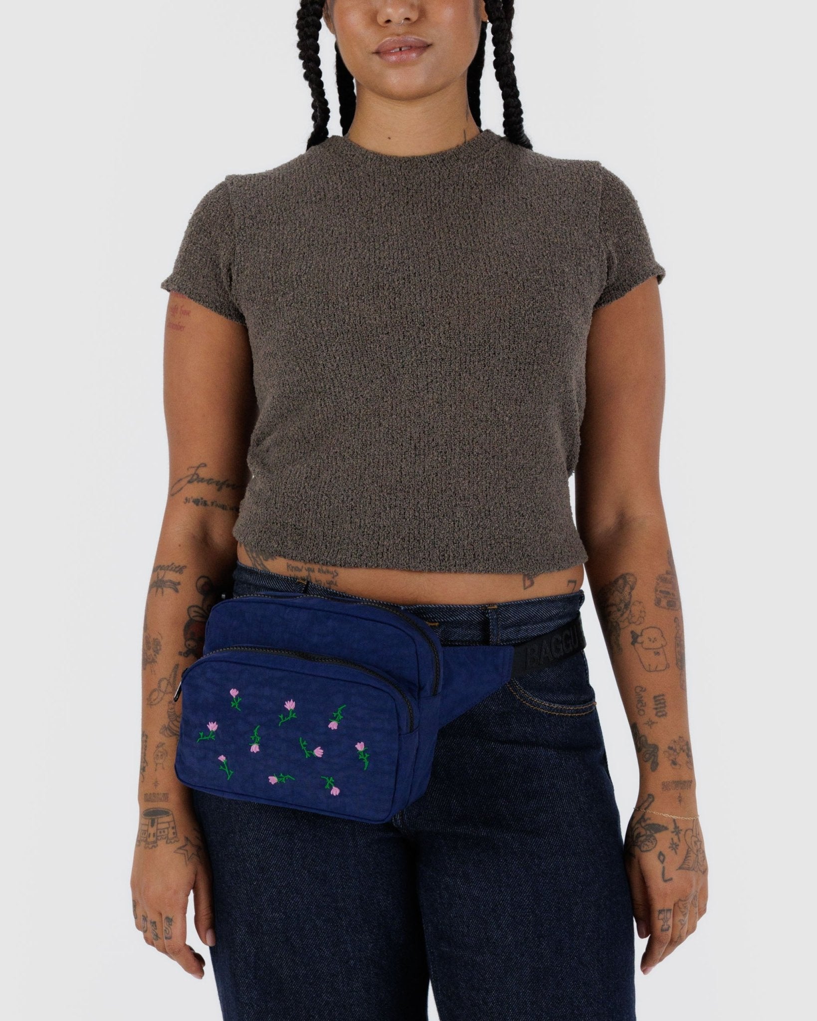 Person wearing a blue fanny pack with floral pink embroidery around waist with adjustable strap.