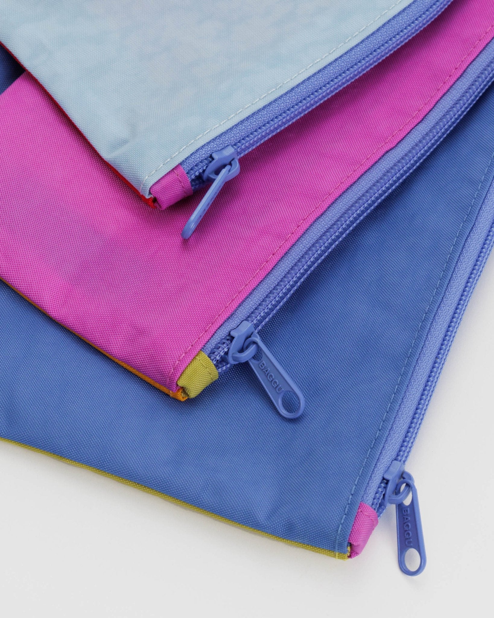 Zips on set of three colourful flat pouches lying flat.