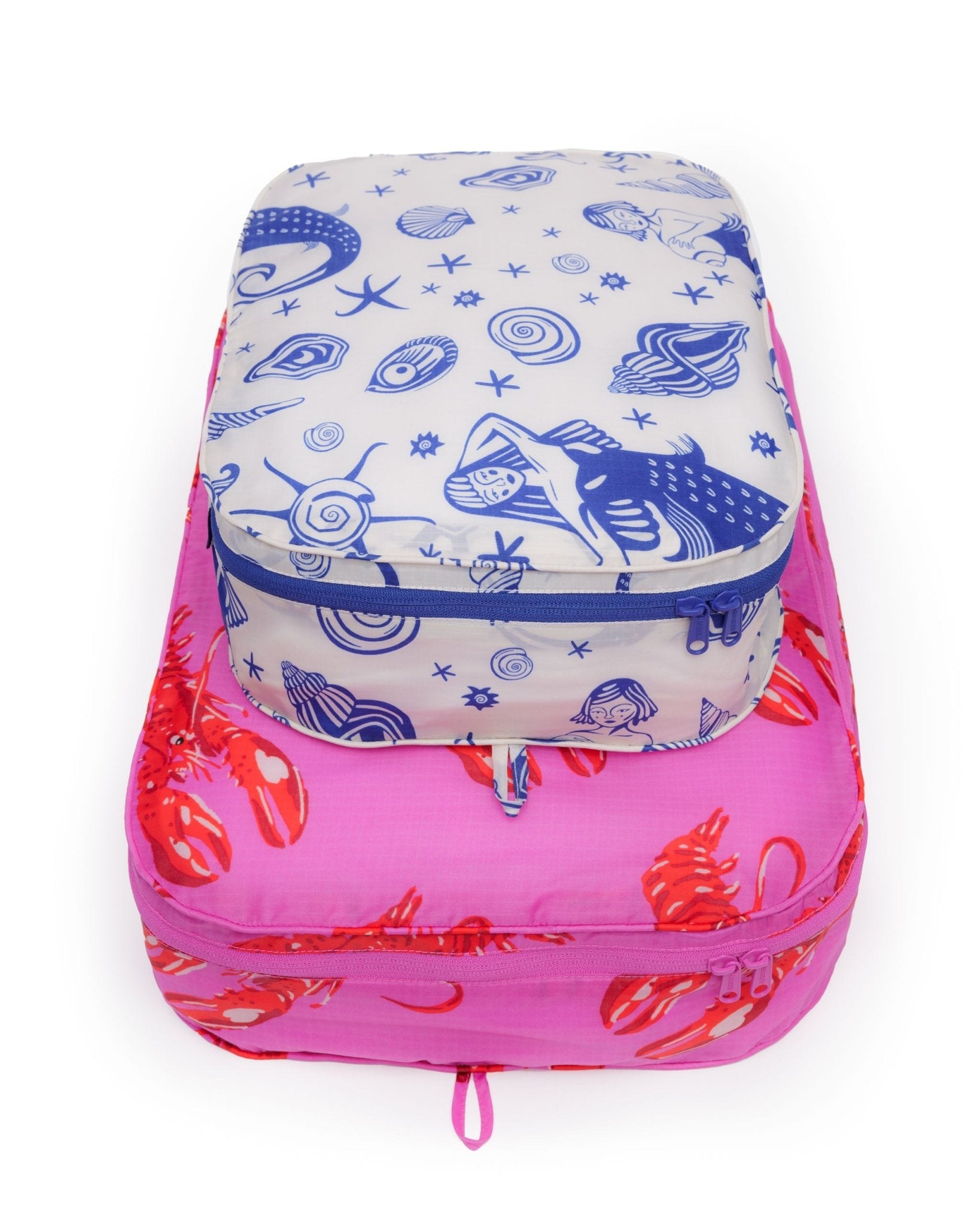 Set of two packed and stacked packing cubes in prints of mermaid and pink lobster with tonal hanging loops.