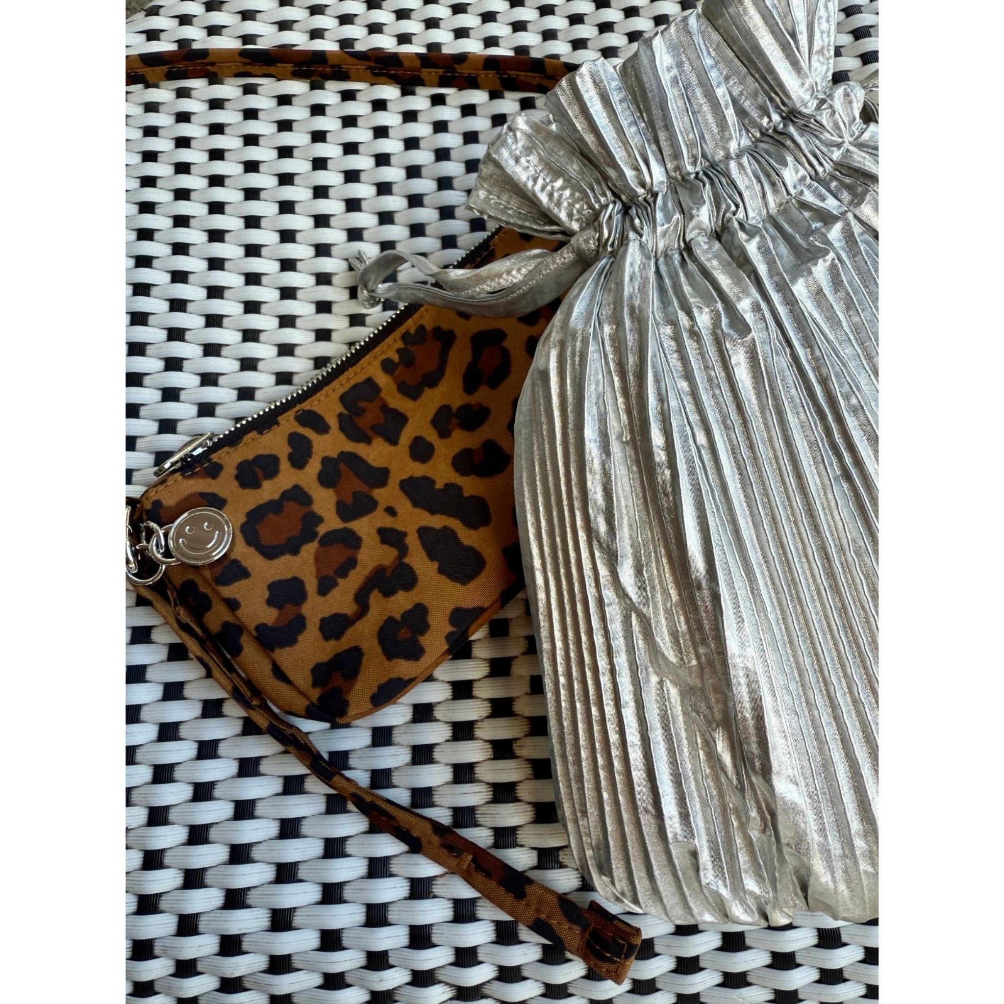 Silver pleated bag and leopard print shoulder bag pochette on a woven chair surface.