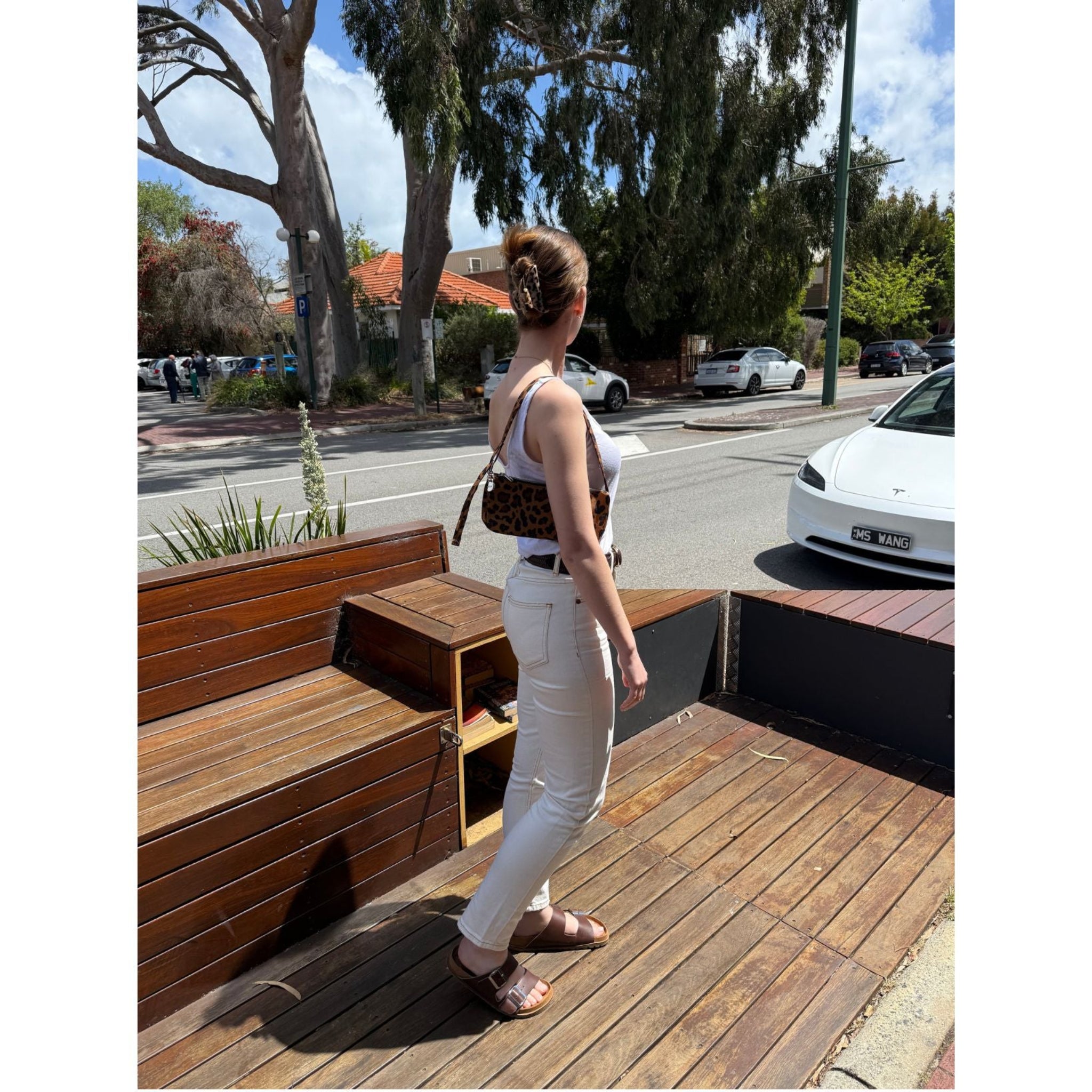 Woman with leopard pochette on shoulder walking on a wooden deck near the street.