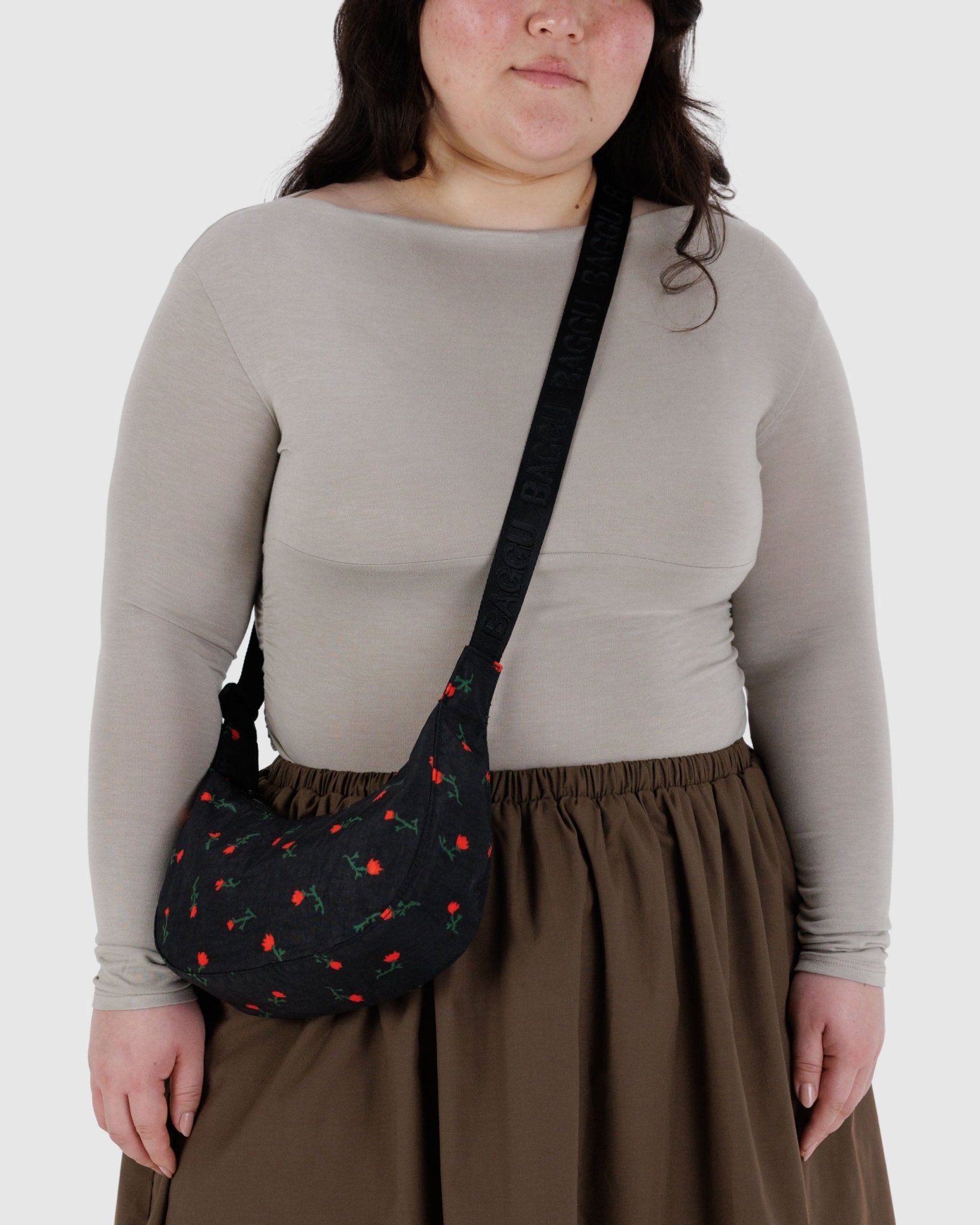 Person wearing a small black crescent shaped crossbody bag with red wildflower patterns