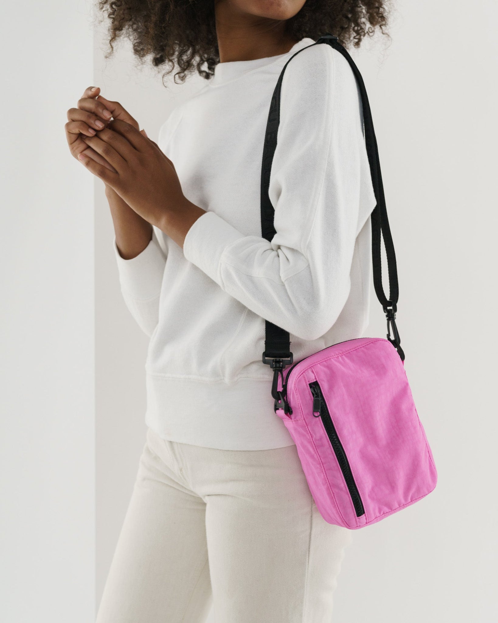 Person wearing a pink crossbody bag on shoulder with black adjustable strap and front and top zip - ANNIE.G