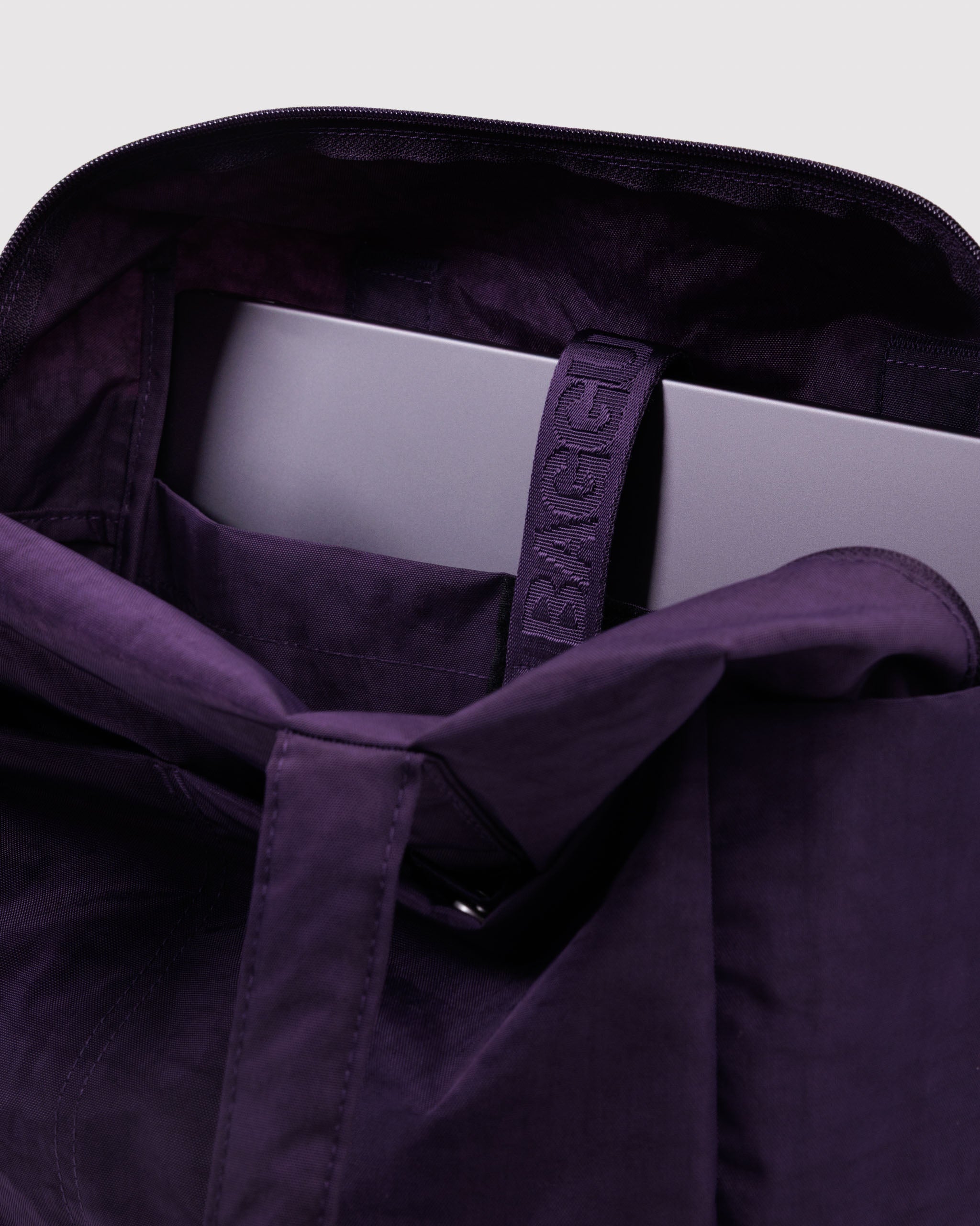 Purple duffle bag with interior tech pocket and laptop inside.