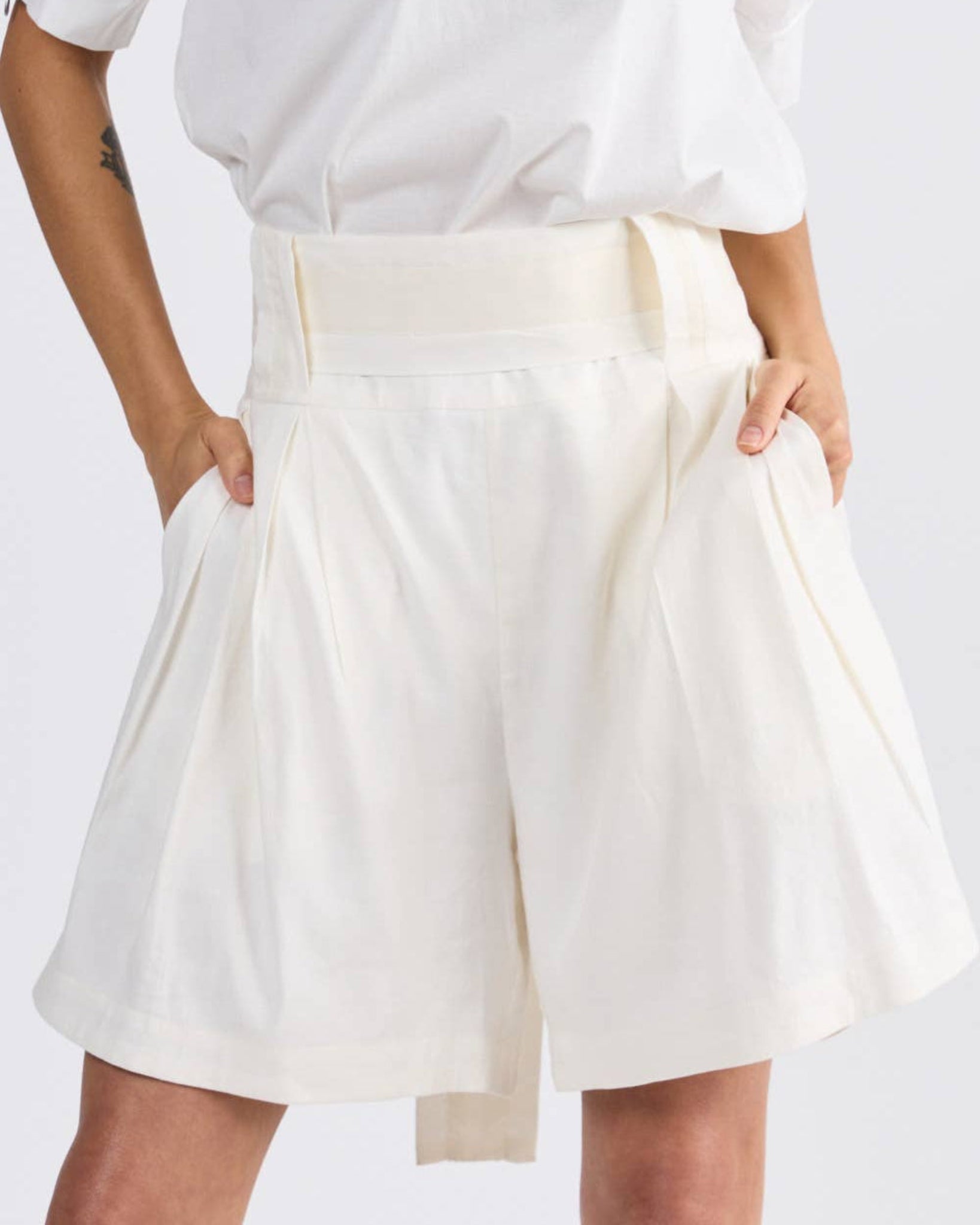 Persons hands in the side pockets of ivory linen shorts and belt through loops hanging at back - ANNIE.G