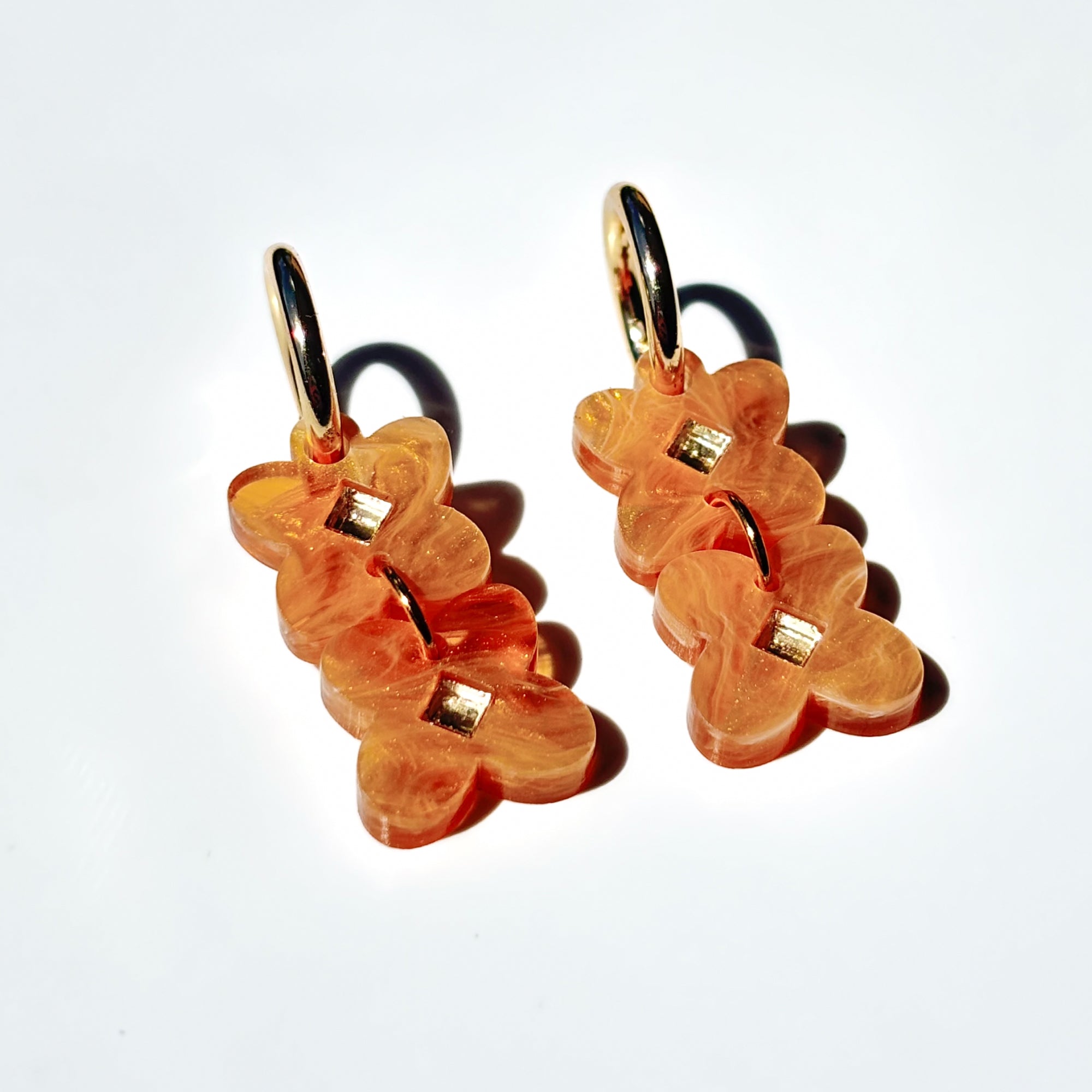 Two sweet clover acrylic flowers inset with gold mirror diamond in light brown acrylic on small gold hoops.