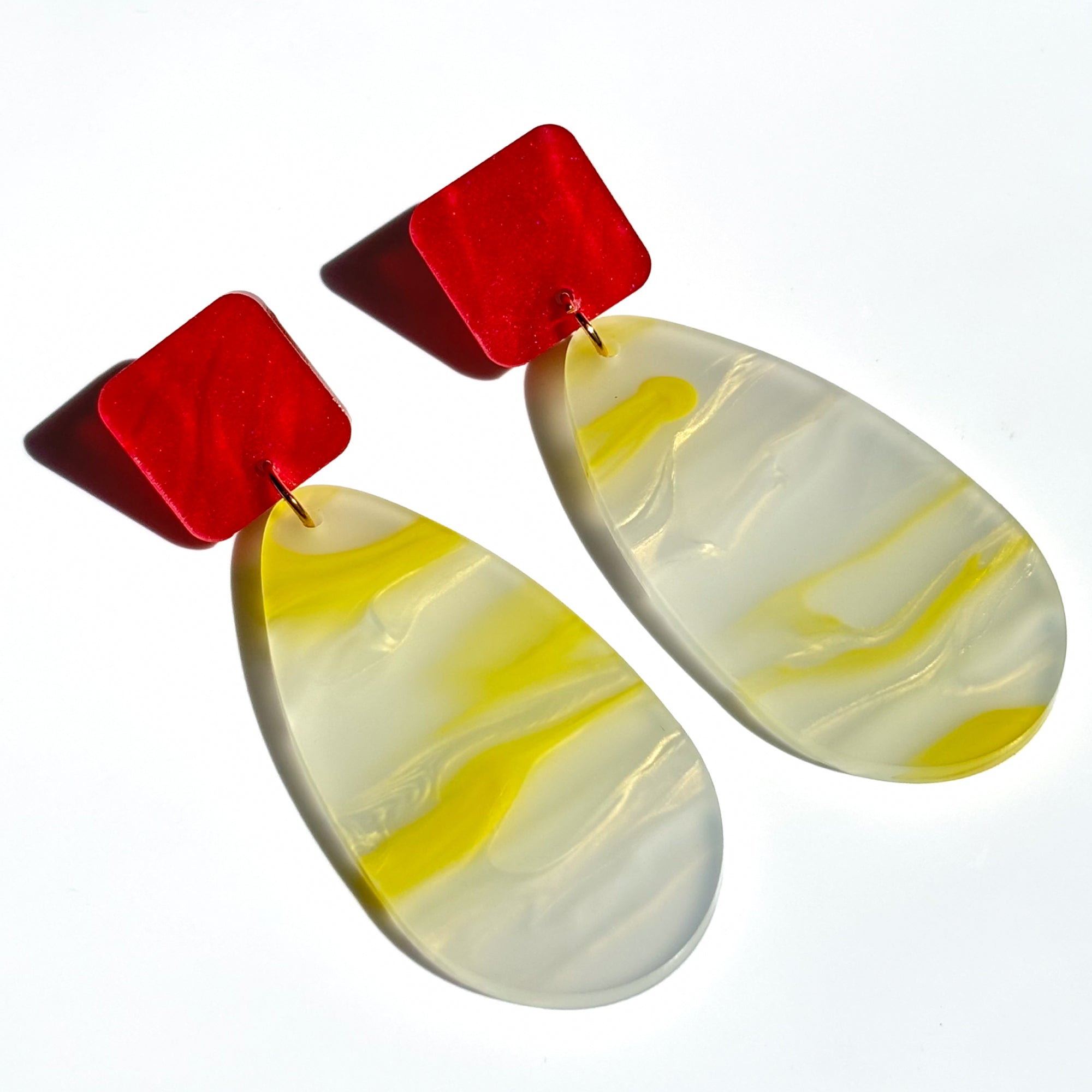 Acrylic dangle earrings in a red square shape at the top and a large tear drop attached in yellow and white swirl colour.