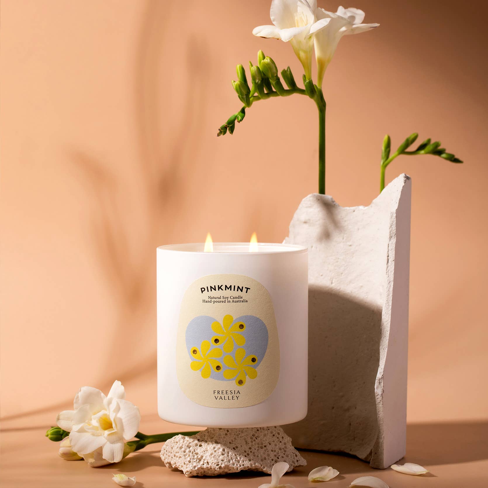 Lit white glass jar candle next to a vase with a white flower - ANNIE.G