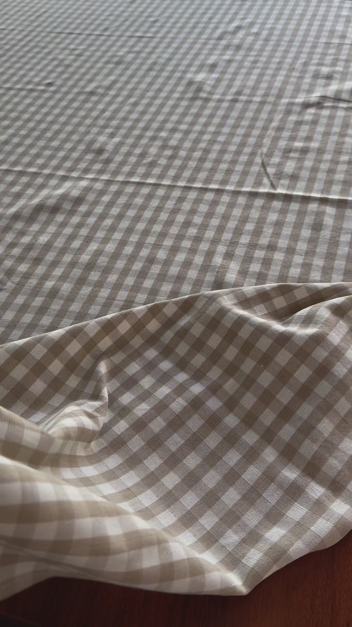 gingham-tablecloth-being-thrown-over-dining-table-hand-knotted-edge