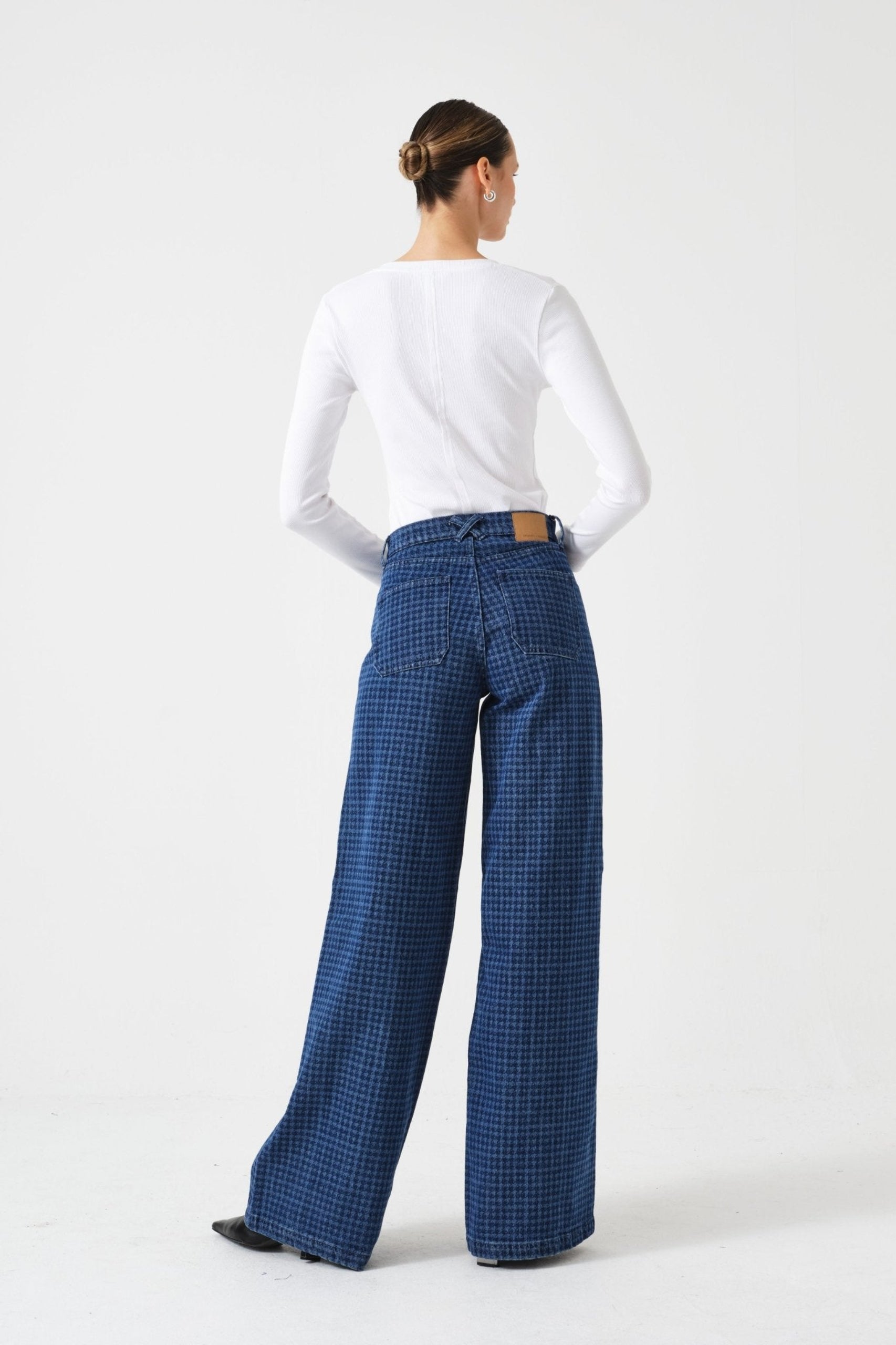 Back of a person wearing blue checkered pants with pockets and a white long-sleeve shirt