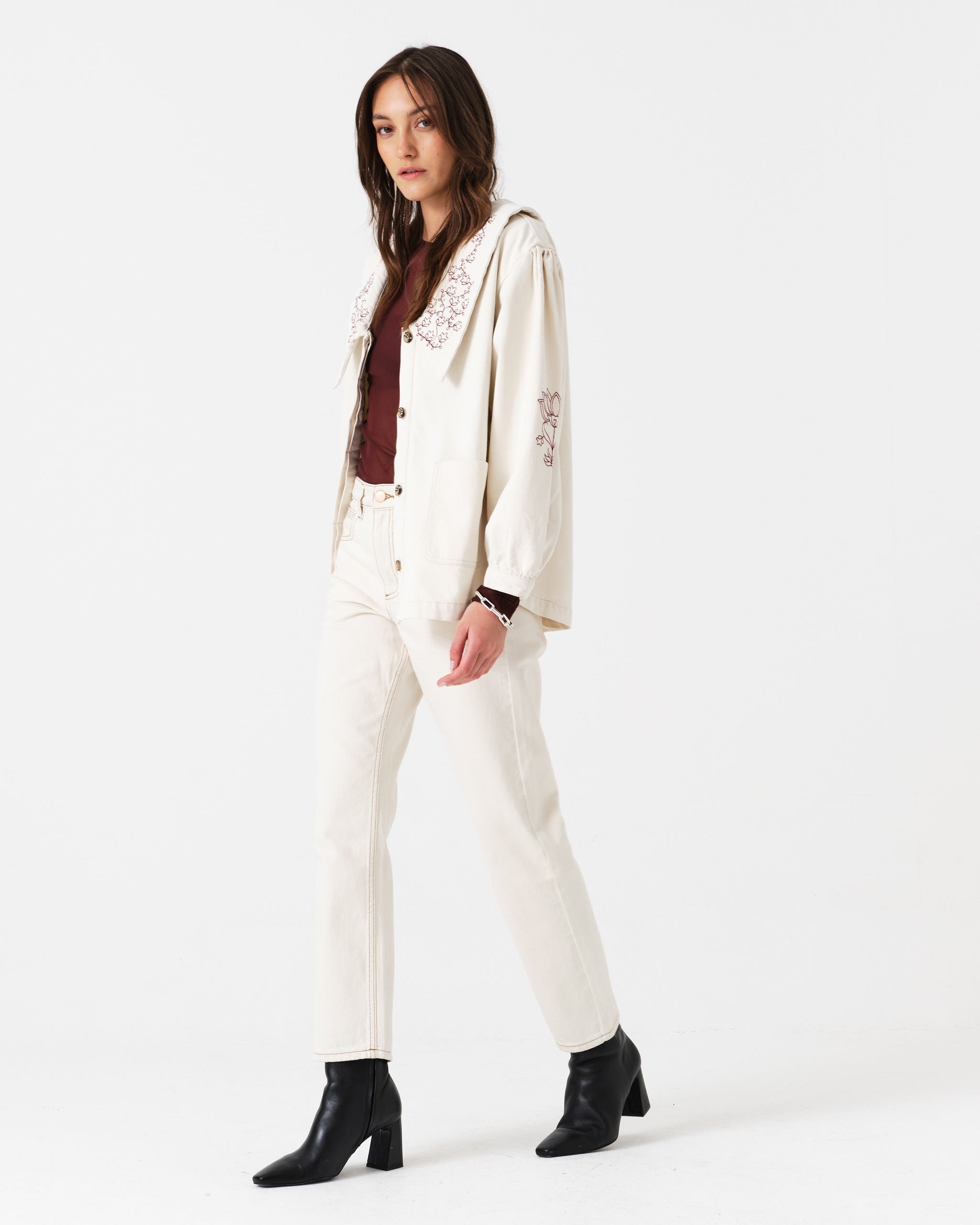 Woman wearing a light cream jacket and jean trousers suit with a brown shirt and black boots.