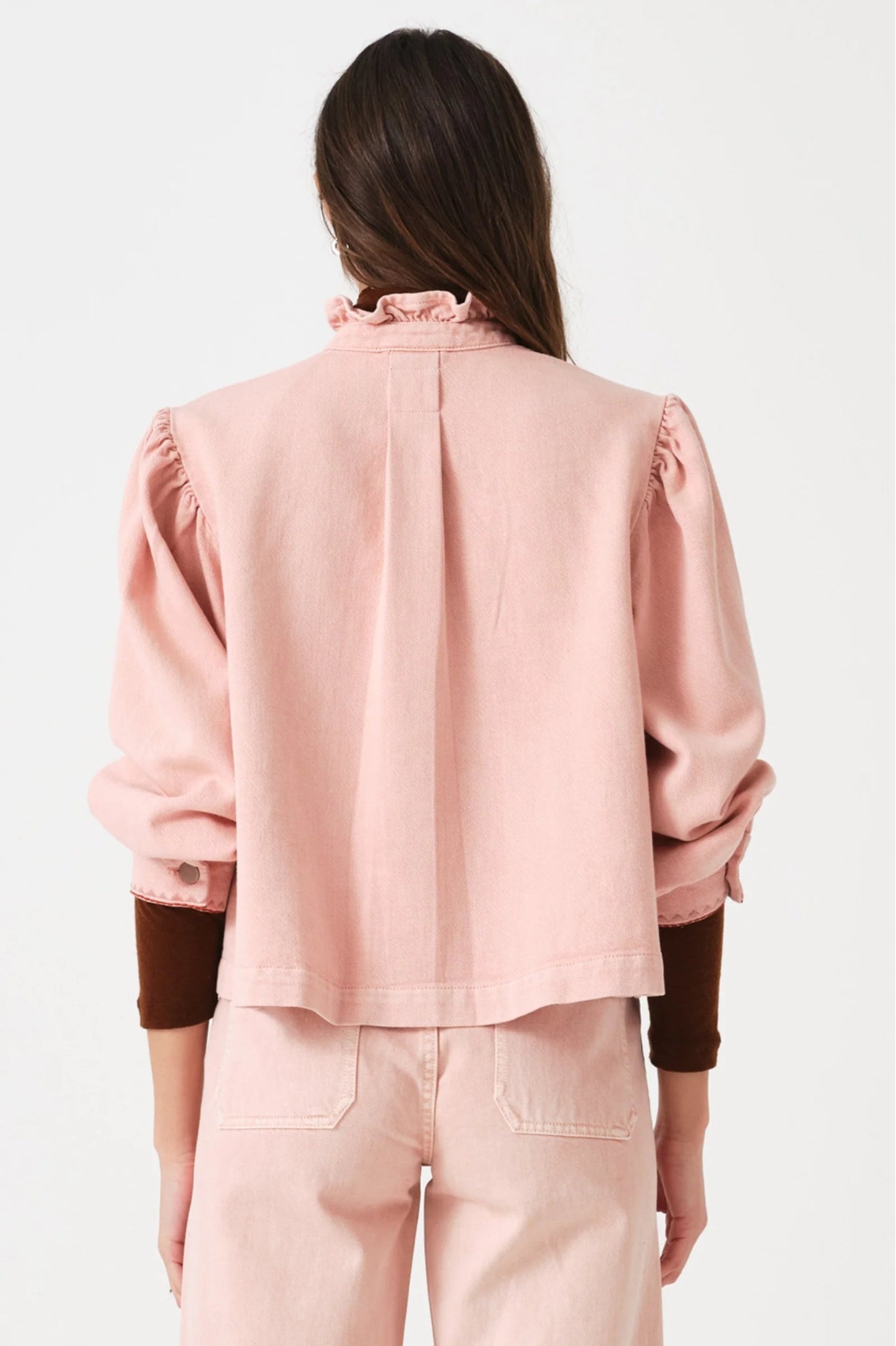 Back of a woman wearing a pink jacket and jeans with pockets outfit with sleeves of maroon top showing