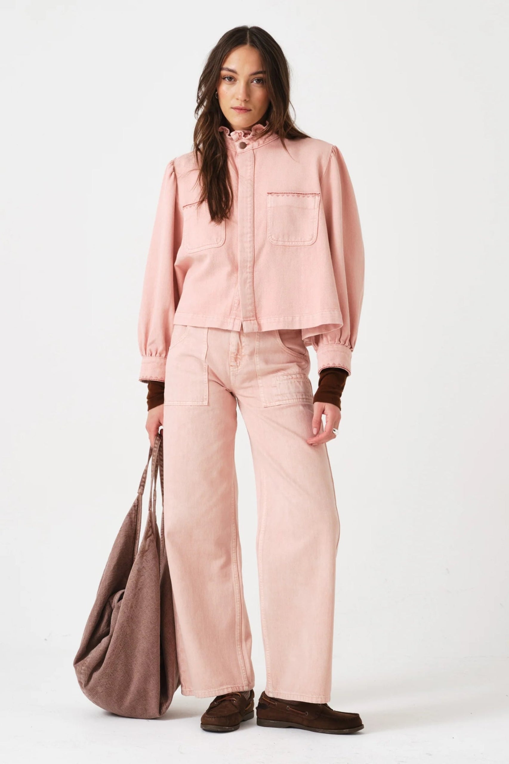 Woman wearing a pink jacket and jeans outfit holding a brown bag