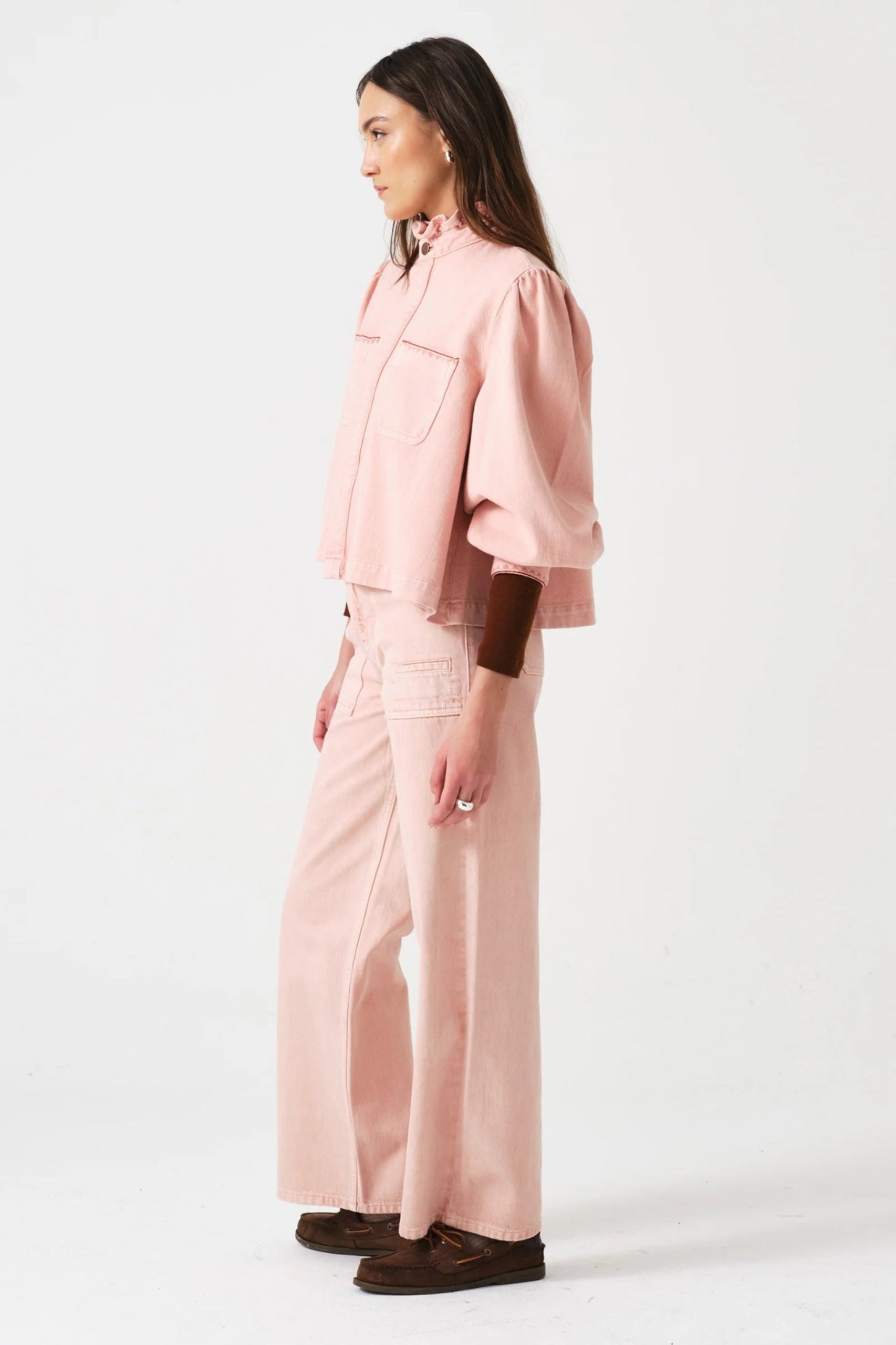 Side of a woman wearing a pink jacket with sleeves pushed up and jeans with patch pockets outfit