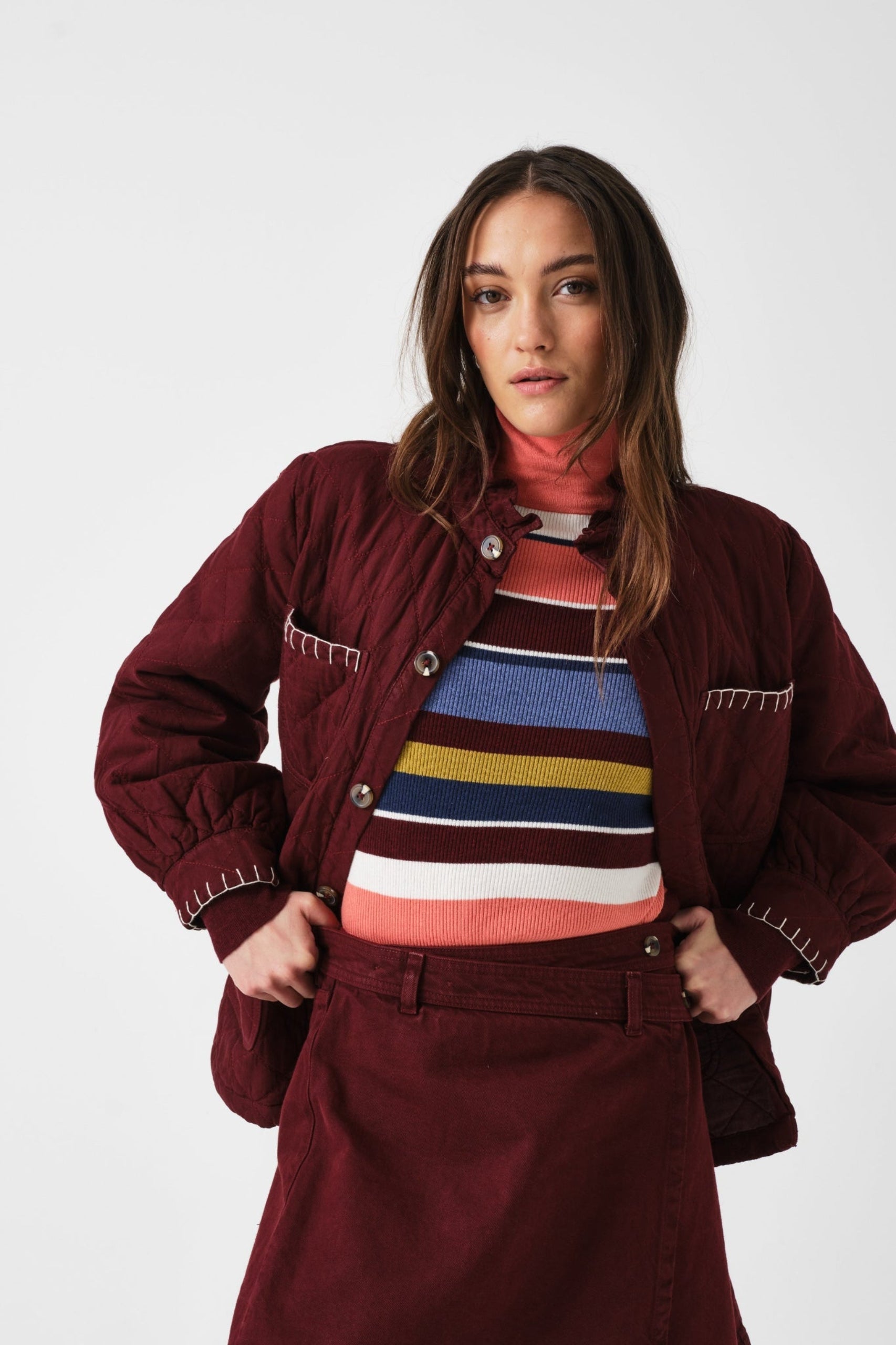 Woman wearing a mulberry jacket and over a striped sweater and mulberry mini wrap skirt.