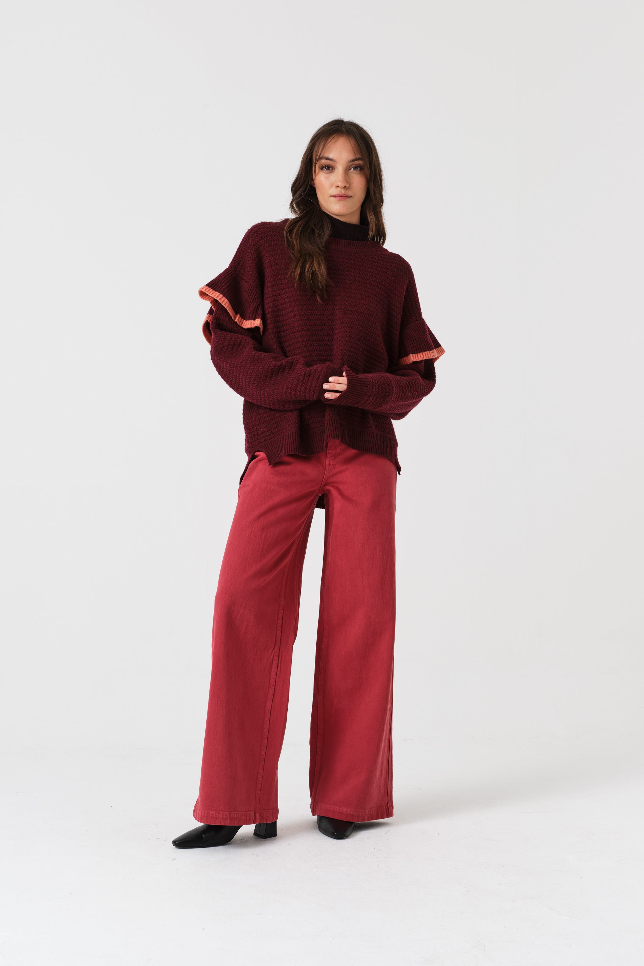Woman wearing a burgundy sweater and faded rose denim jeans.