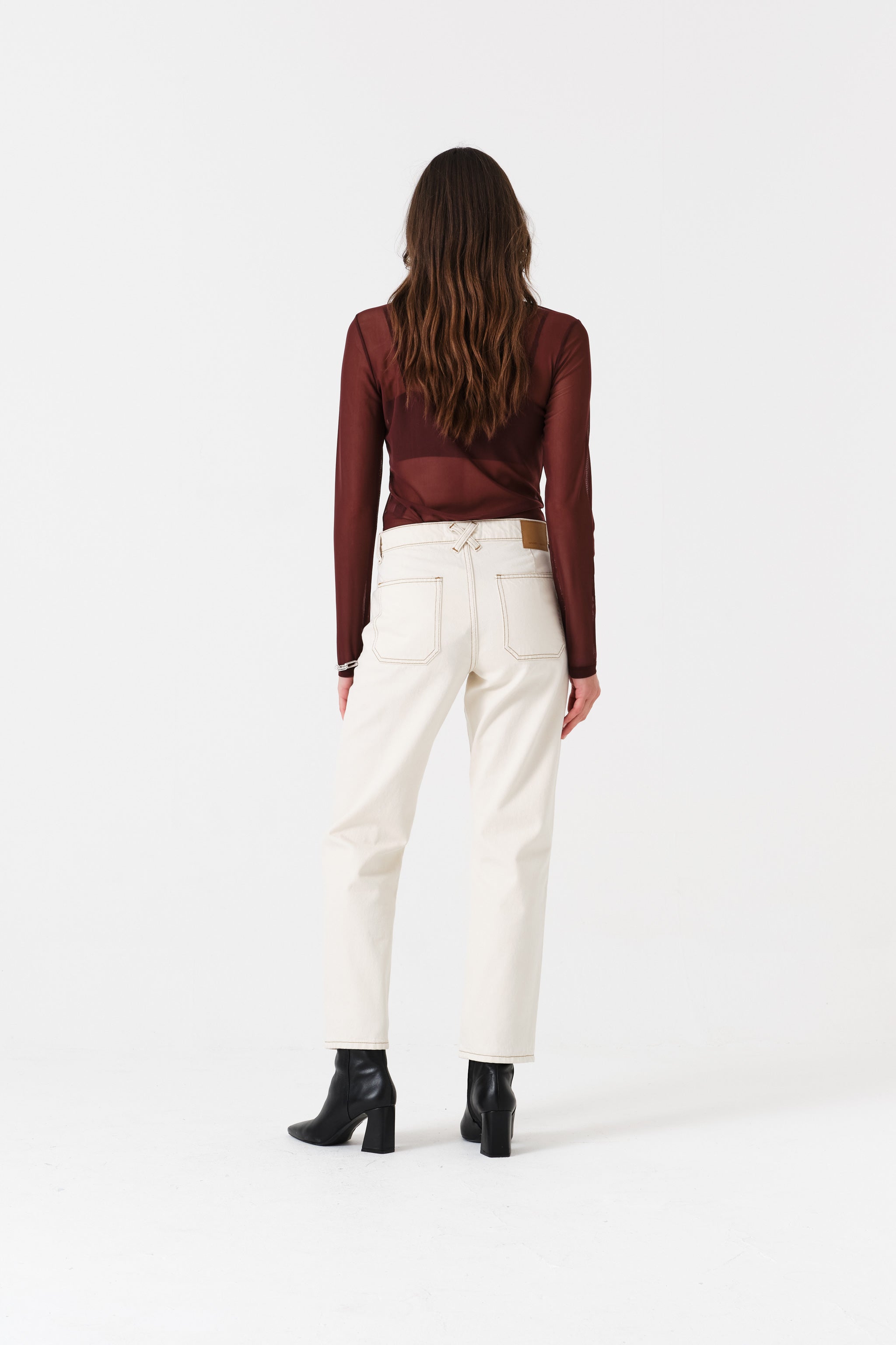 Back of woman wearing a burgundy top and white cotton jeans.