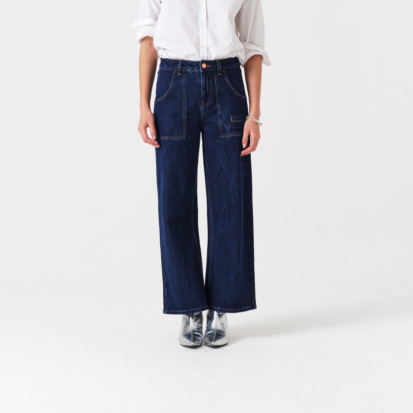 Person wearing cropped blue jeans with retro patch pockets and a white shirt.