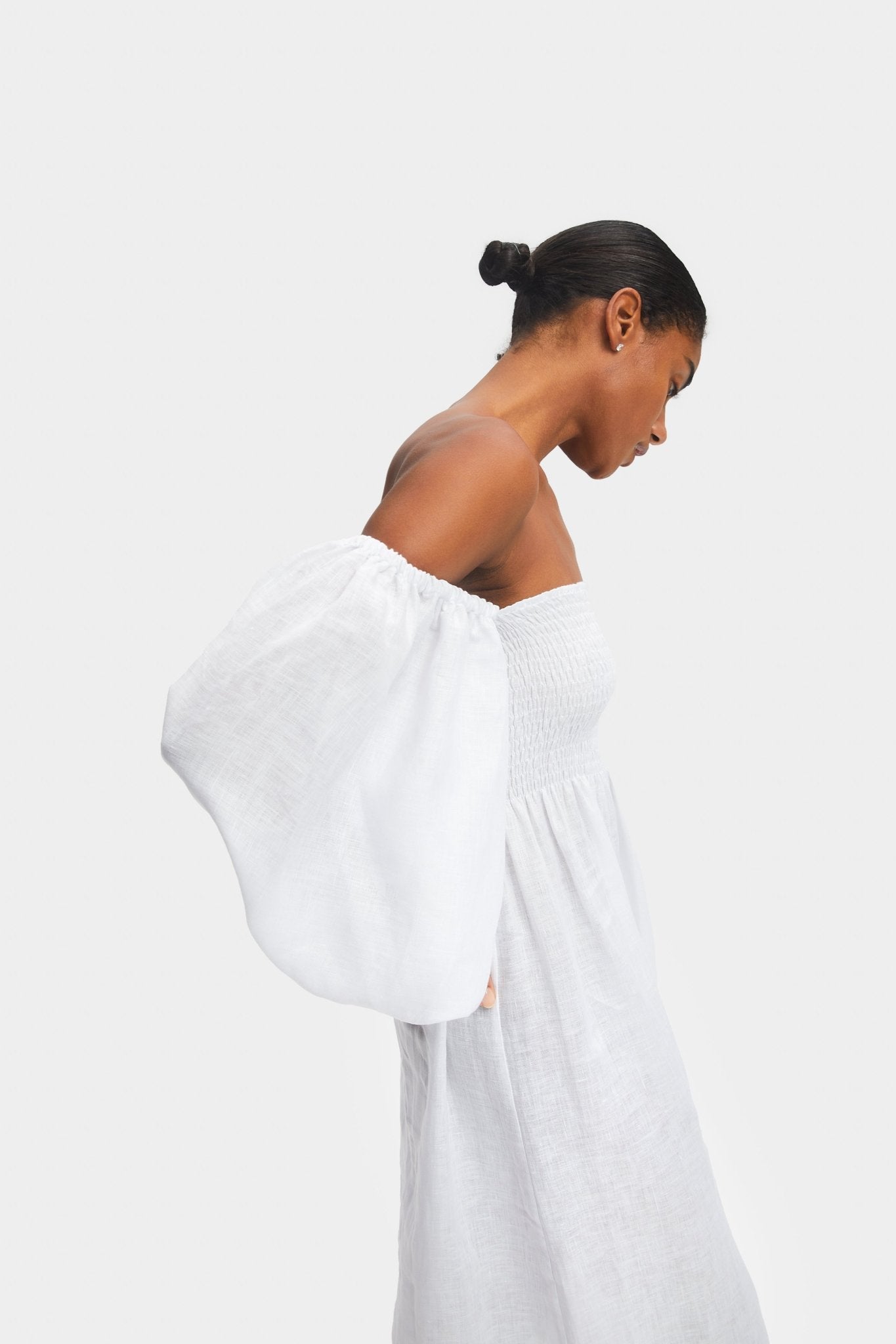 Woman wearing a white off the shoulder dress with long puff sleeves.