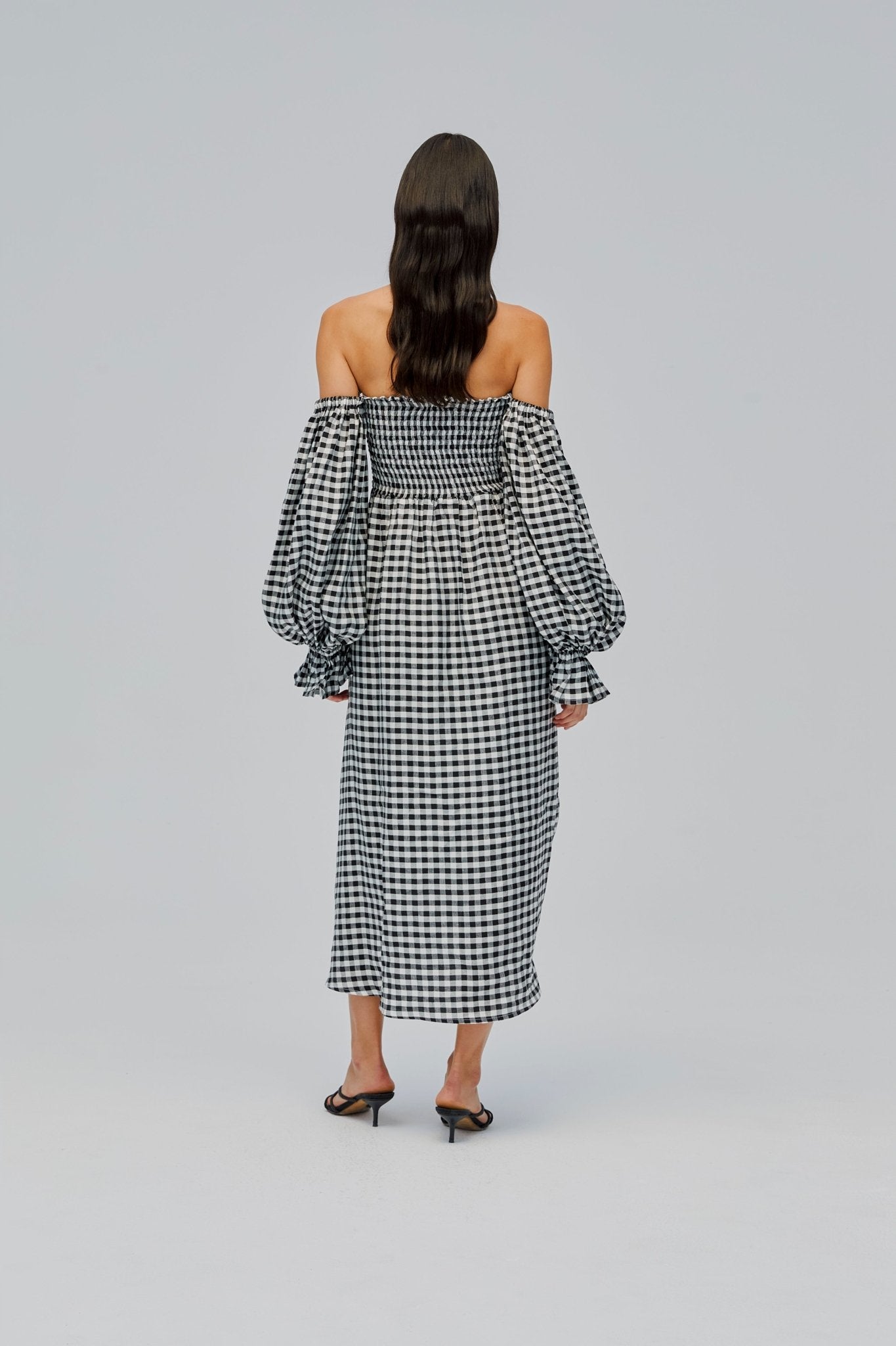 Back of a woman wearing a smocked black and white gingham linen dress with long puff sleeves.