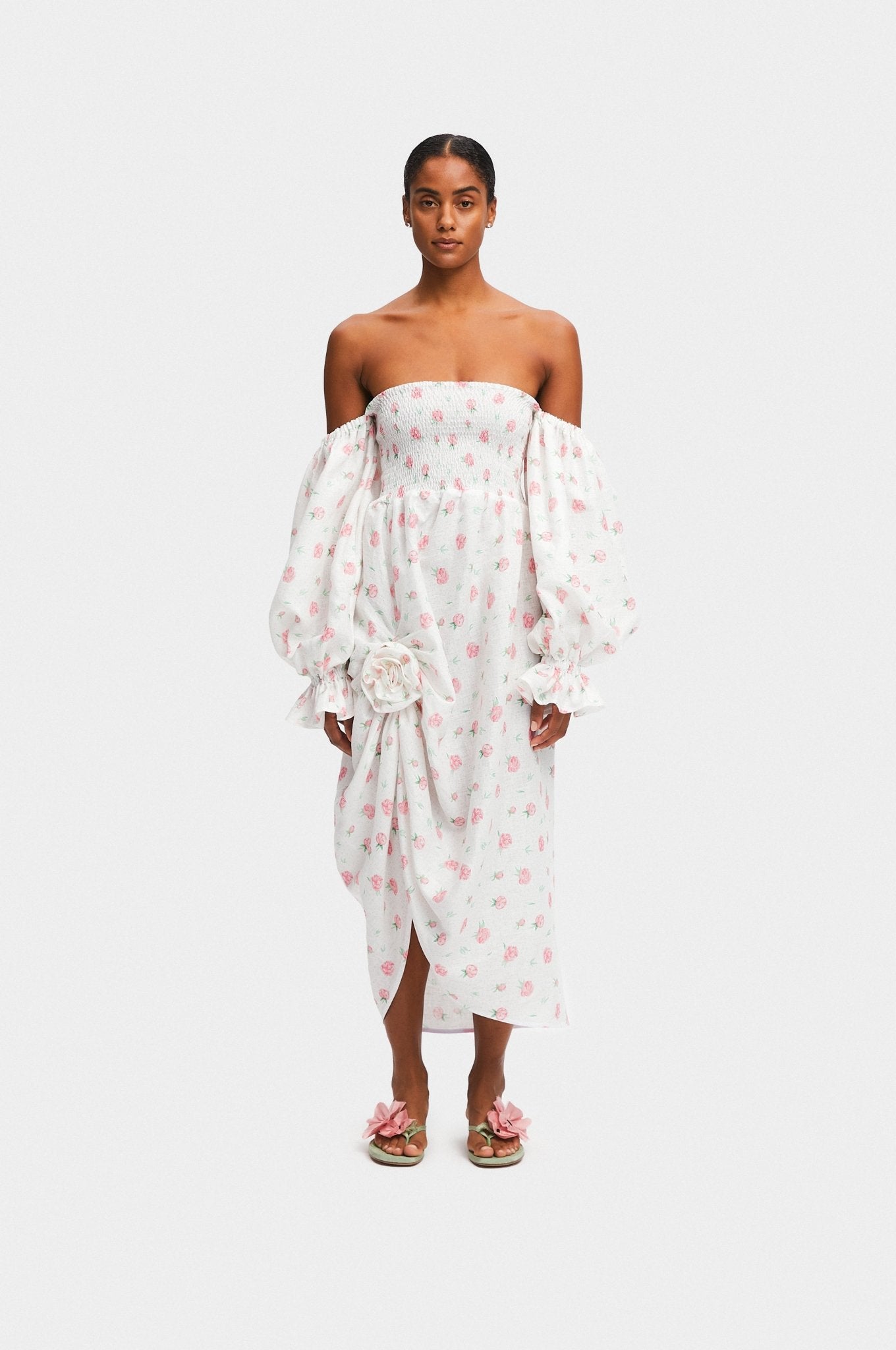 Woman wearing a white linen dress with Rose Detail in Roses with long sleeves off the shoulders and poppy shoes.