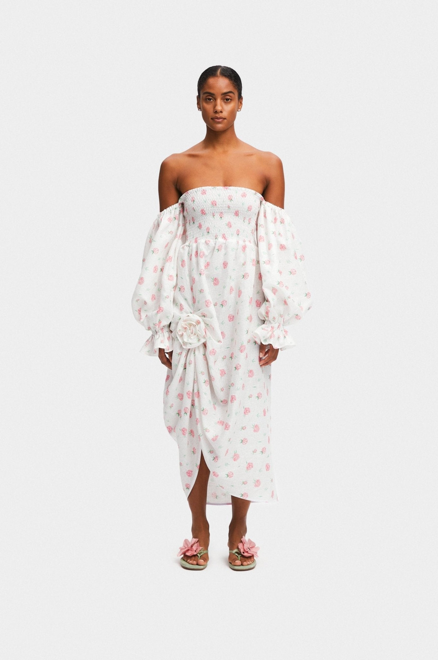 Woman wearing a white linen dress with Rose Detail in Roses with long sleeves off the shoulders and poppy shoes.