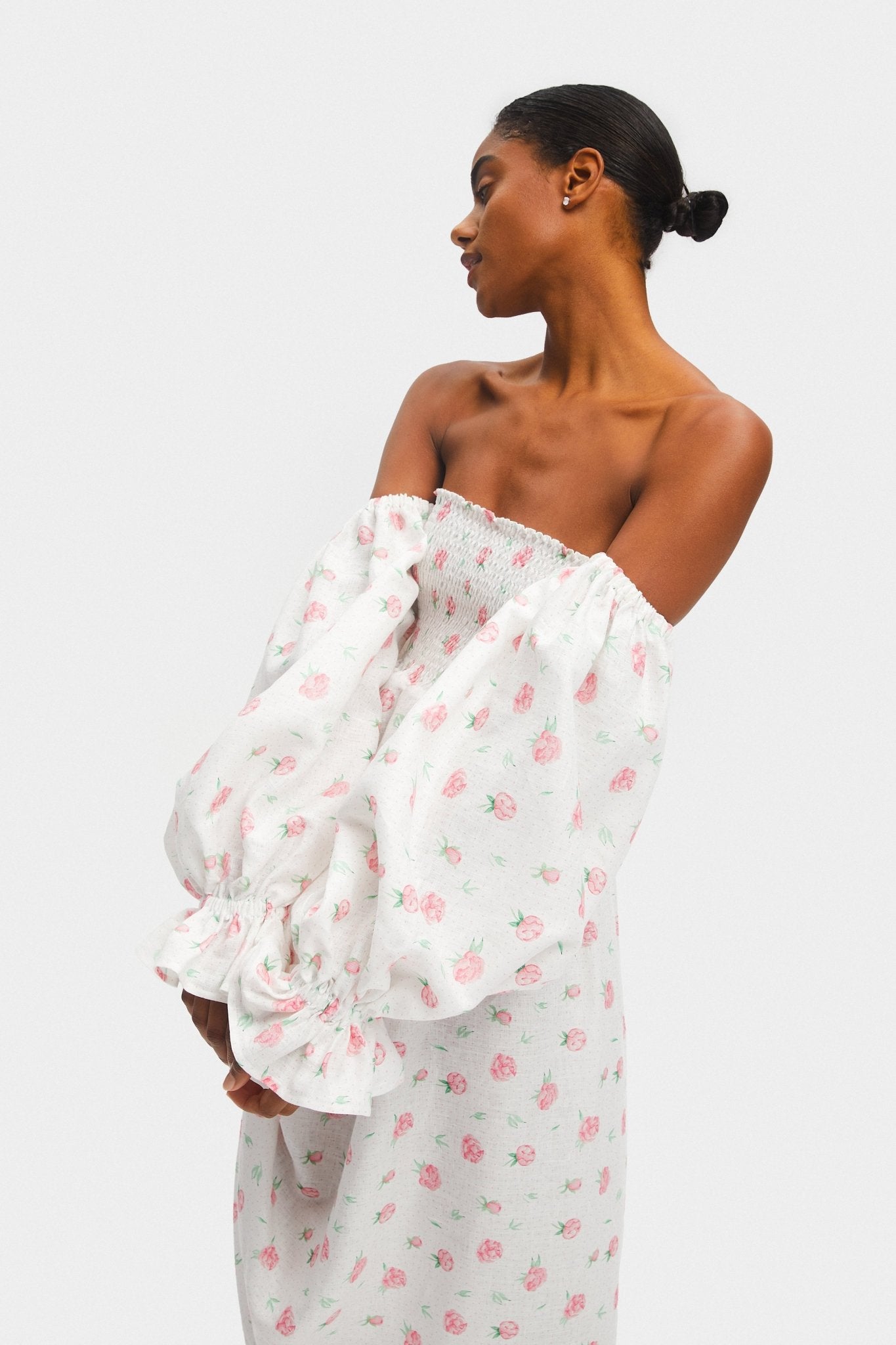 Long sleeves worn off the shoulder with elasticated cuffs on a white linen dress in roses.